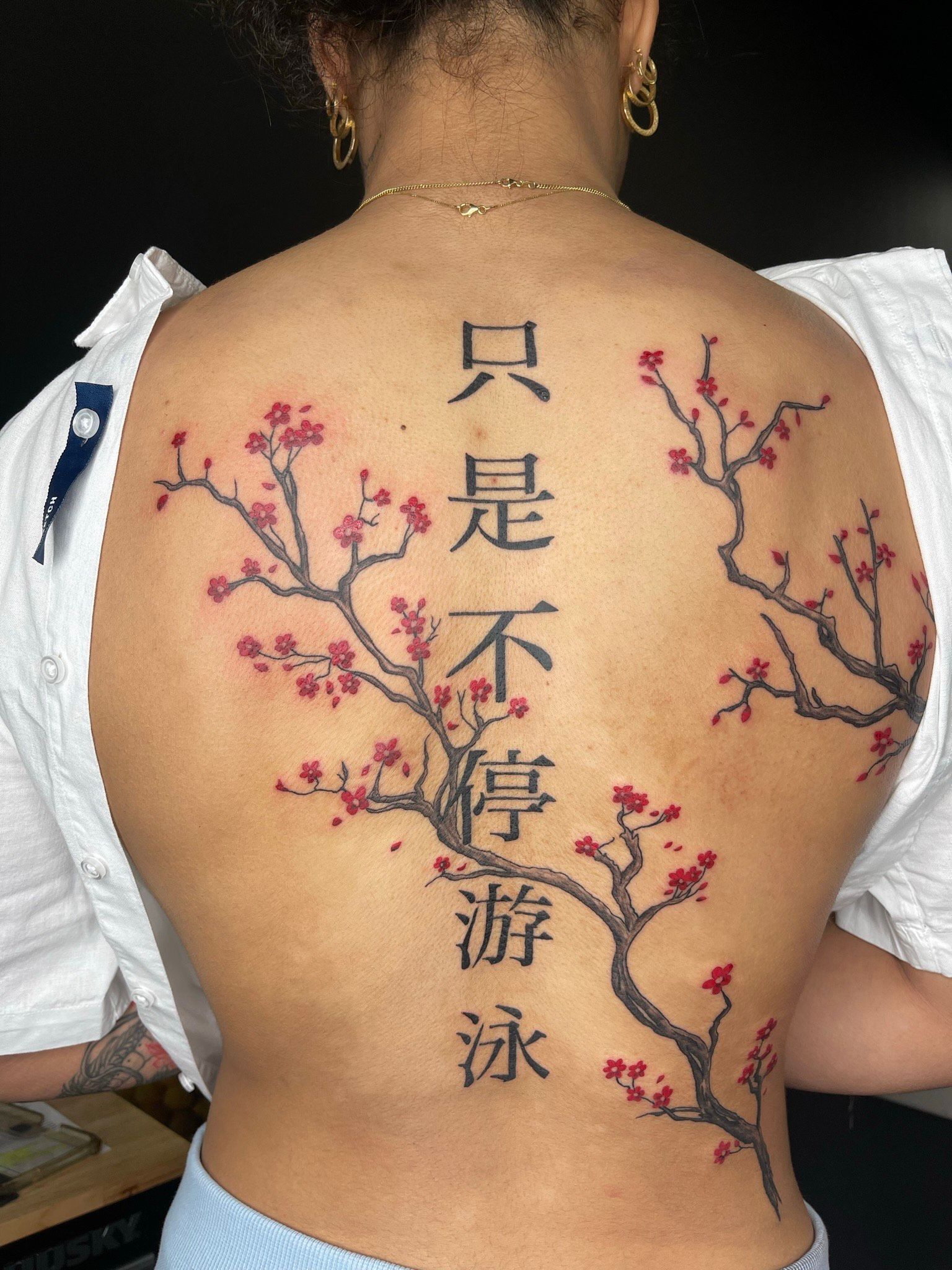 A woman has a cherry blossom tree tattoo on her back.