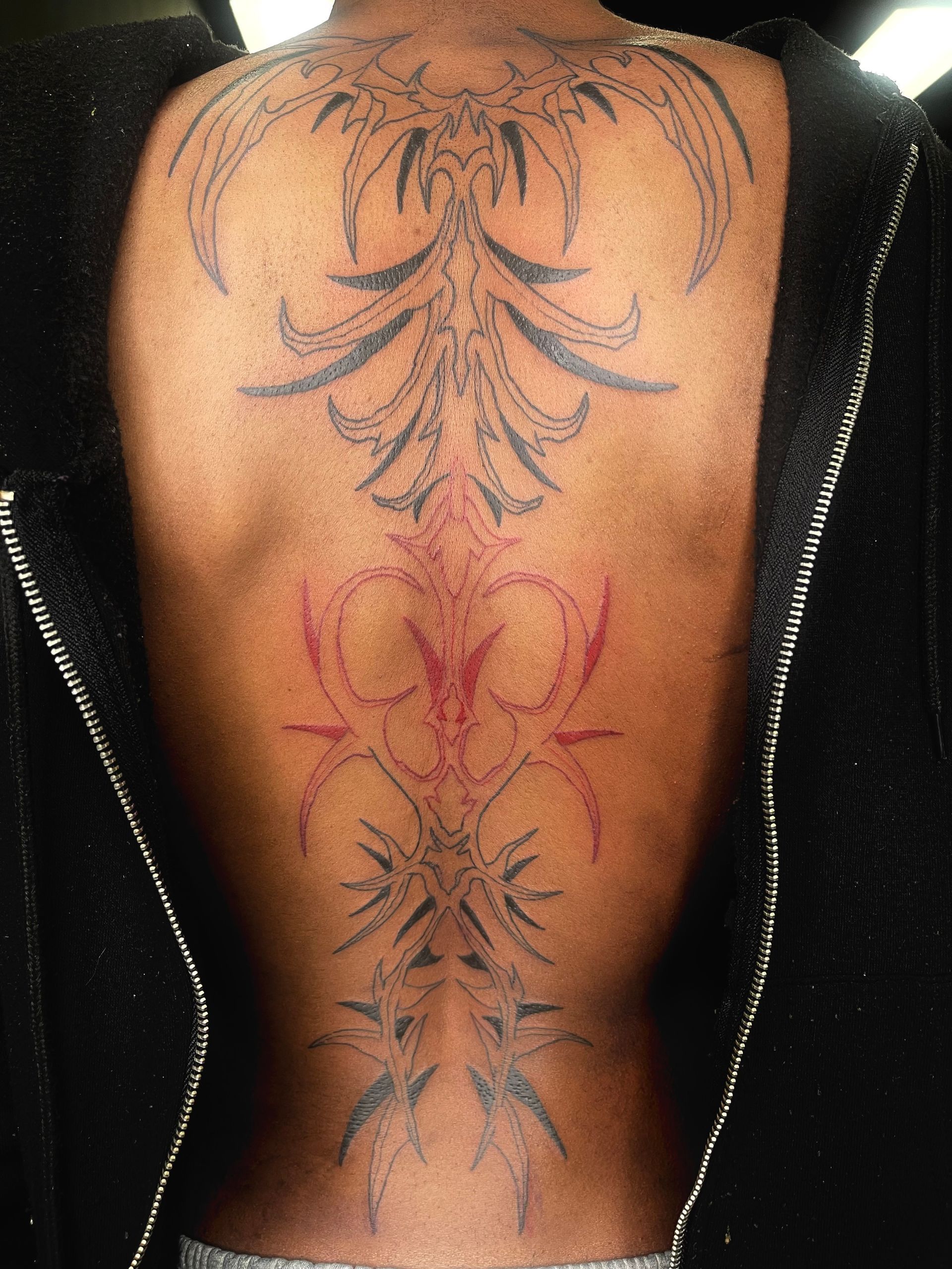 A man with a tattoo on his back is wearing a black jacket