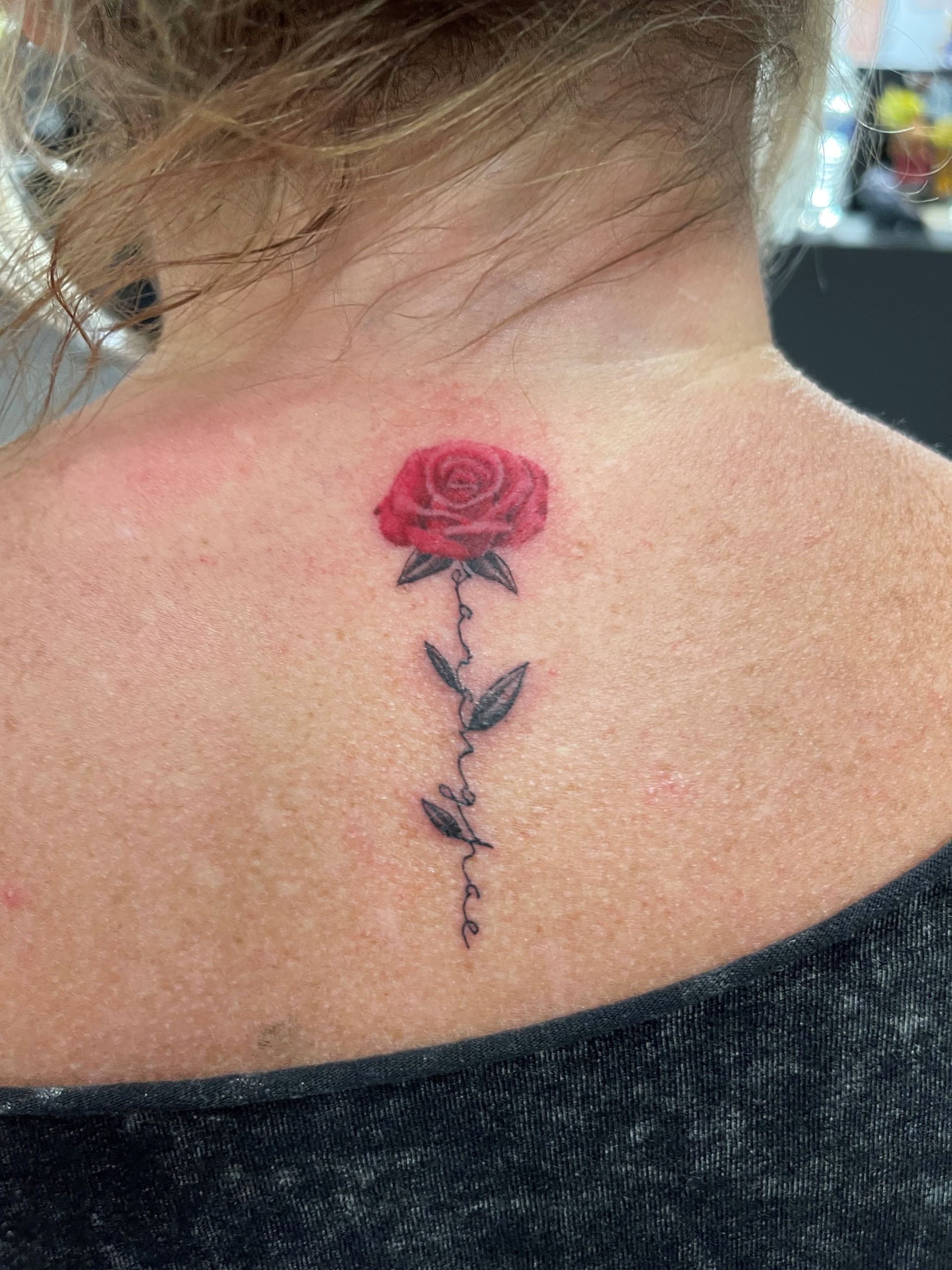 A woman has a red rose tattoo on the back of her neck.