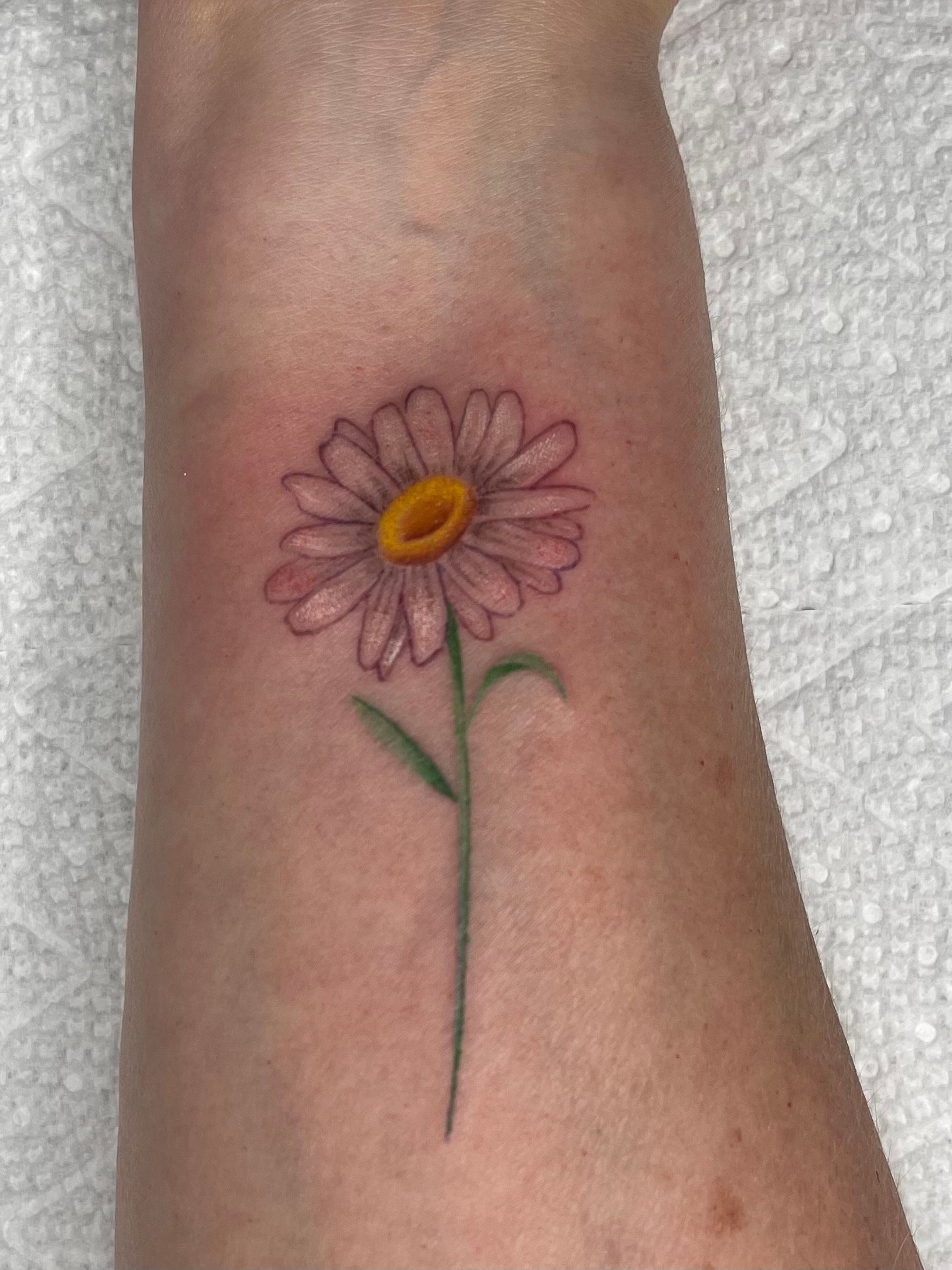 A small tattoo of a daisy on a person 's wrist.