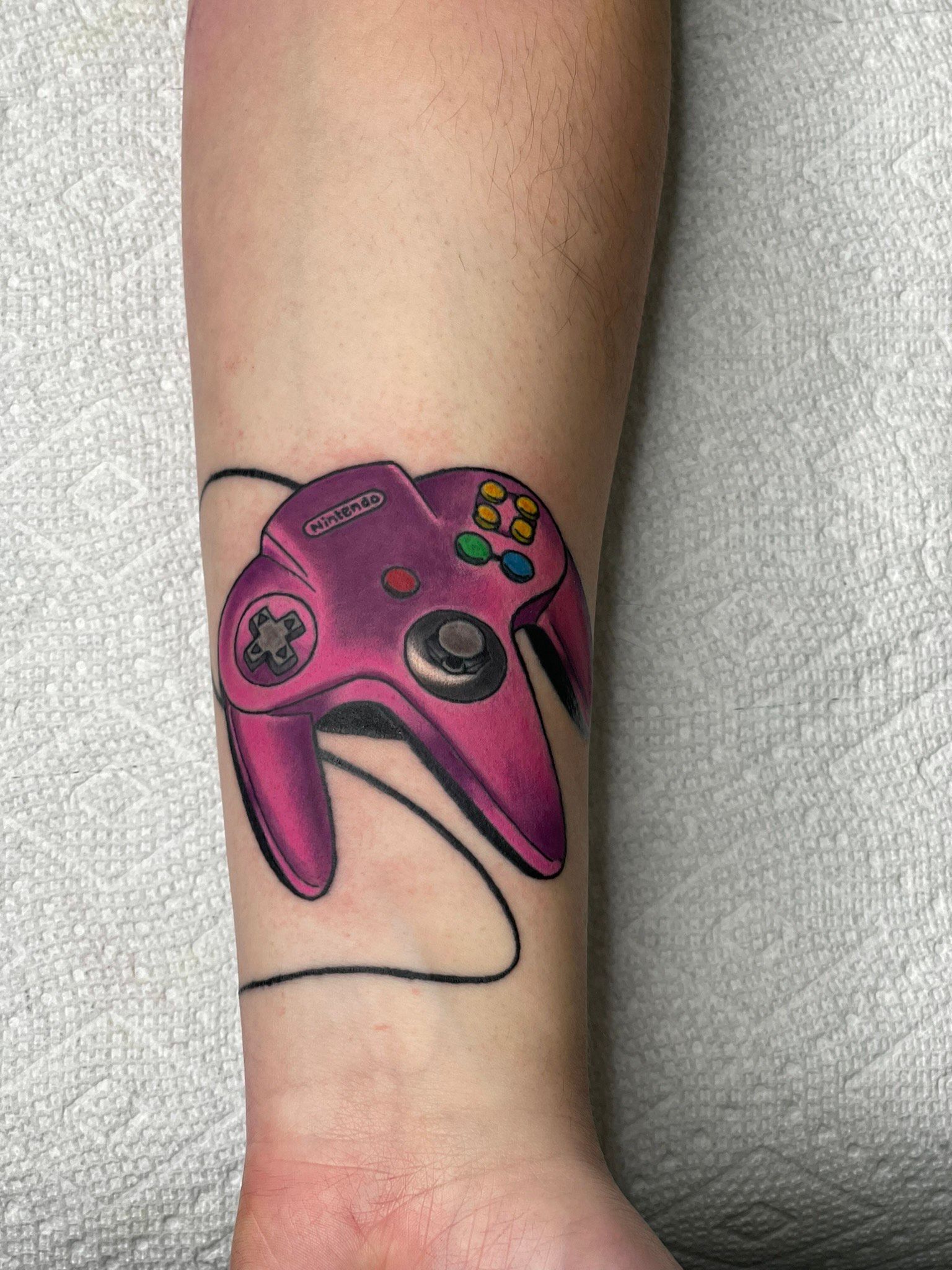 A person has a tattoo of a pink video game controller on their wrist.