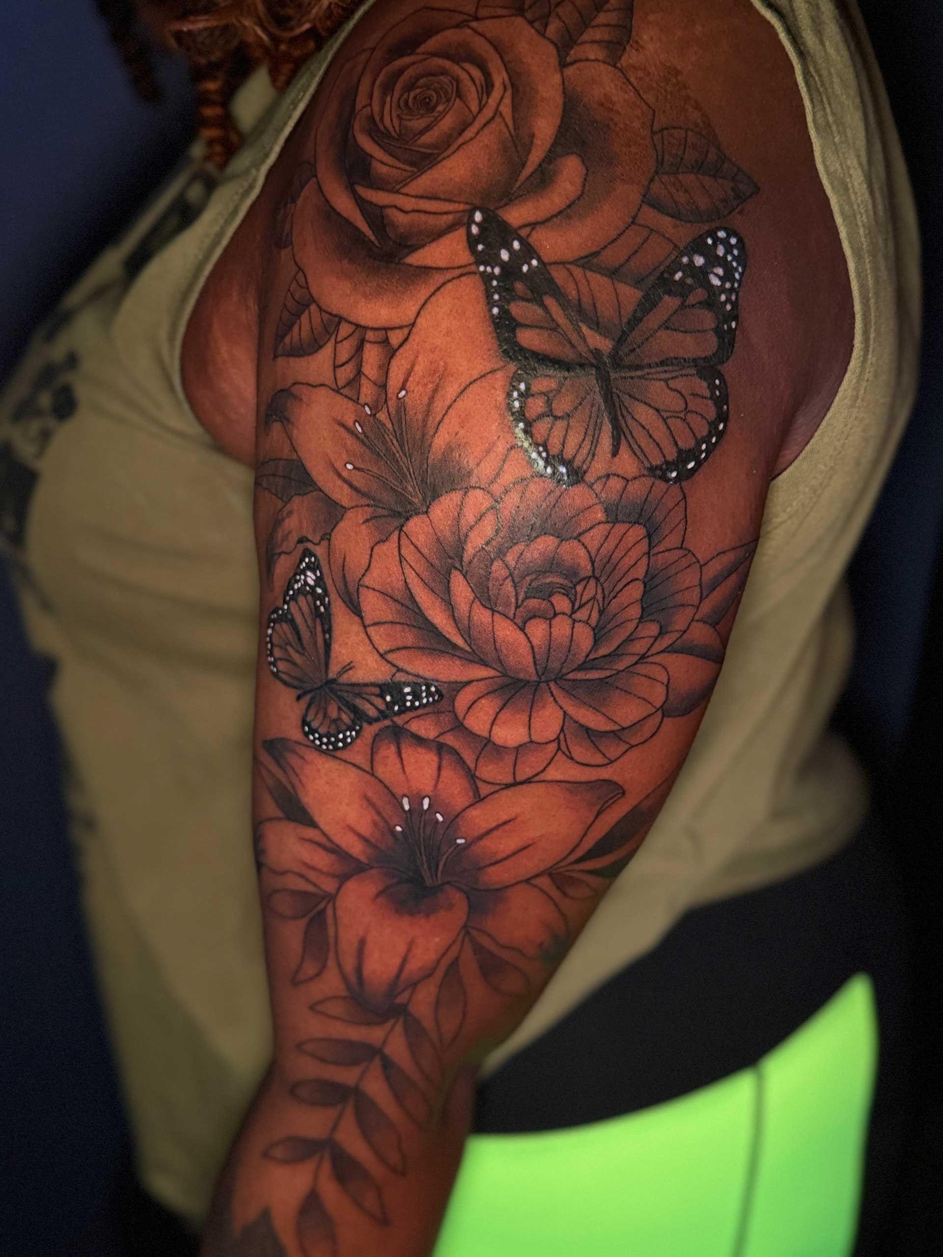 Floral and butterfly tattoo on a person's upper arm and shoulder, with red and black shading