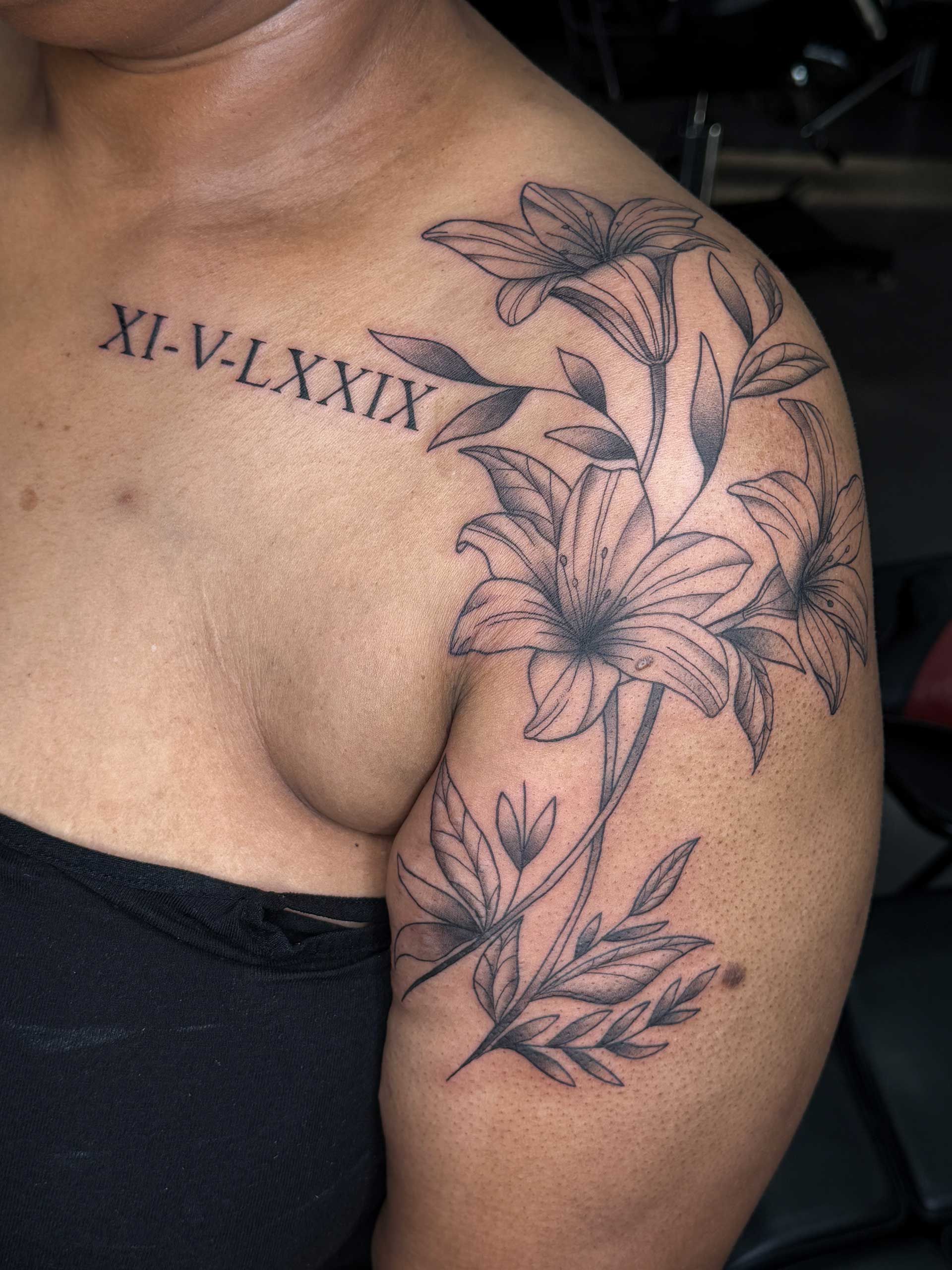 Shoulder and upper arm tattoo of flowers and leaves with Roman numerals across the chest