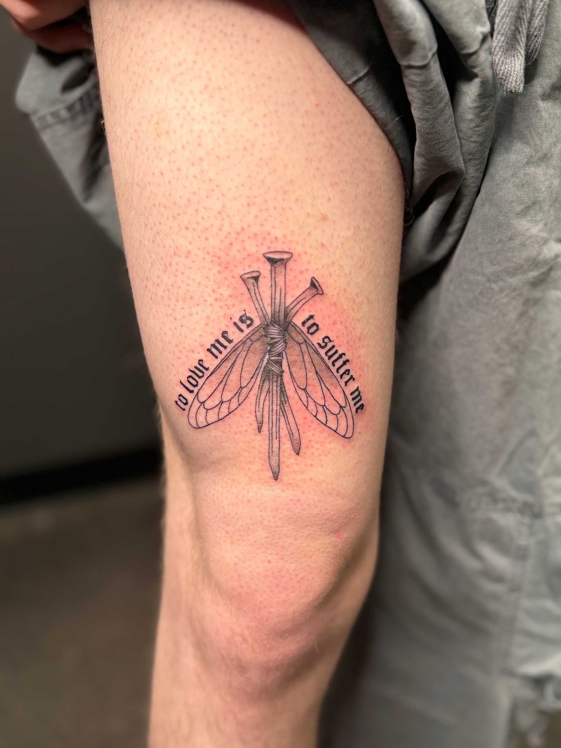 Close-up of a tattooed forearm with a black dragonfly design and surrounding text