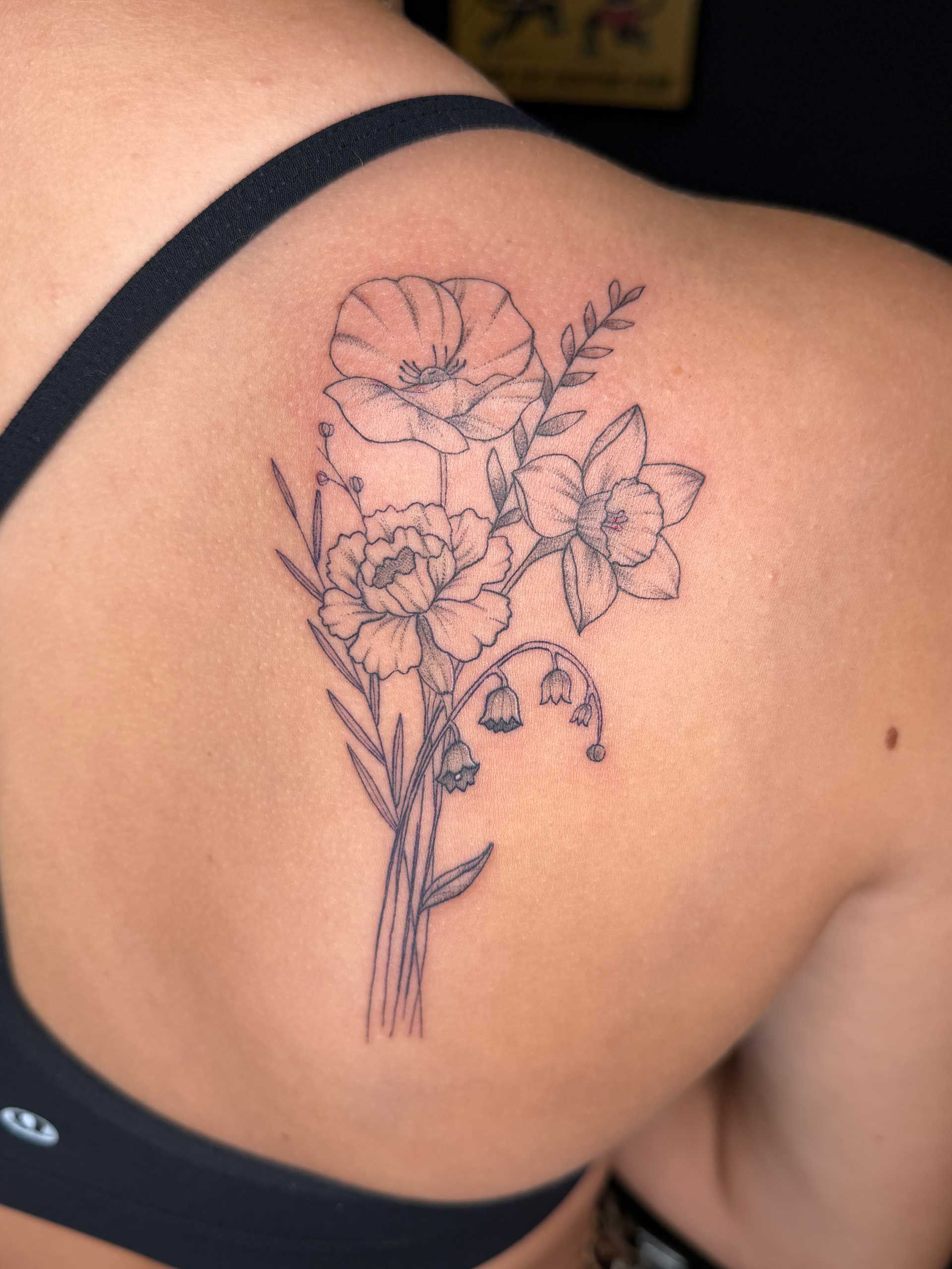 Floral linework tattoo on a shoulder blade, black ink on skin