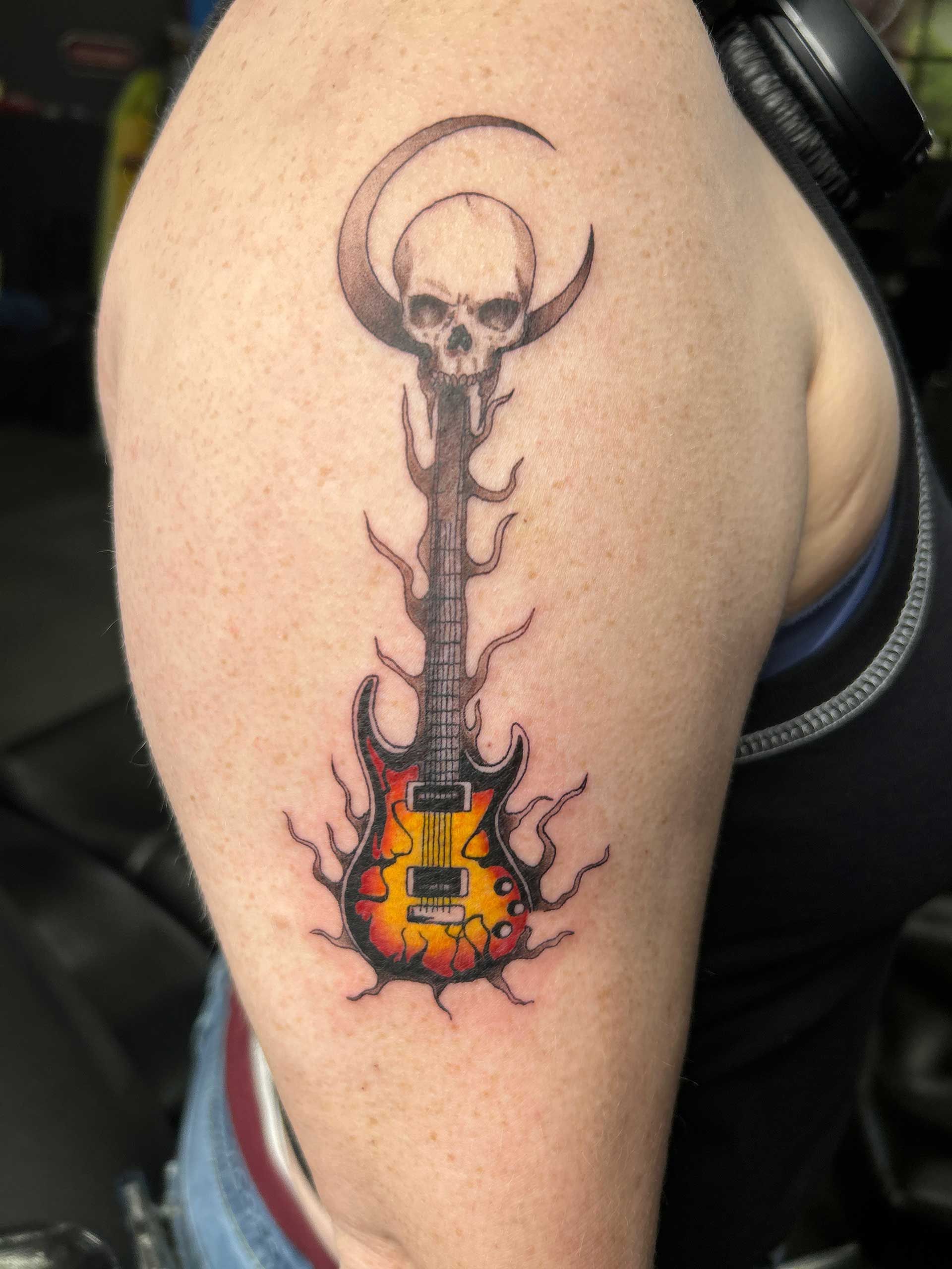 Tattoo of a black skull-topped electric guitar with orange flames on skin
