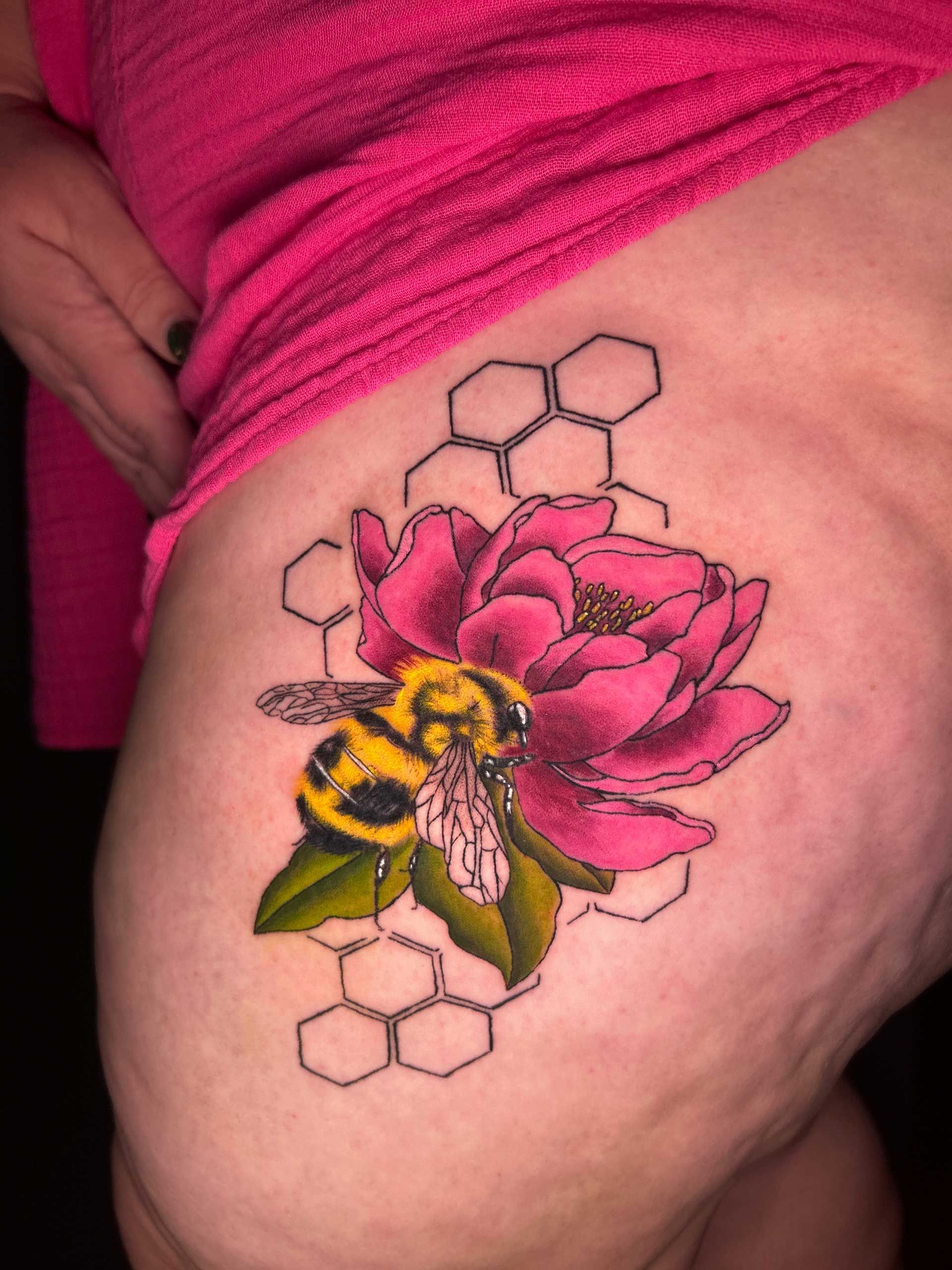 Pink flower and yellow bee tattoo on a hip, with hexagon outlines on skin
