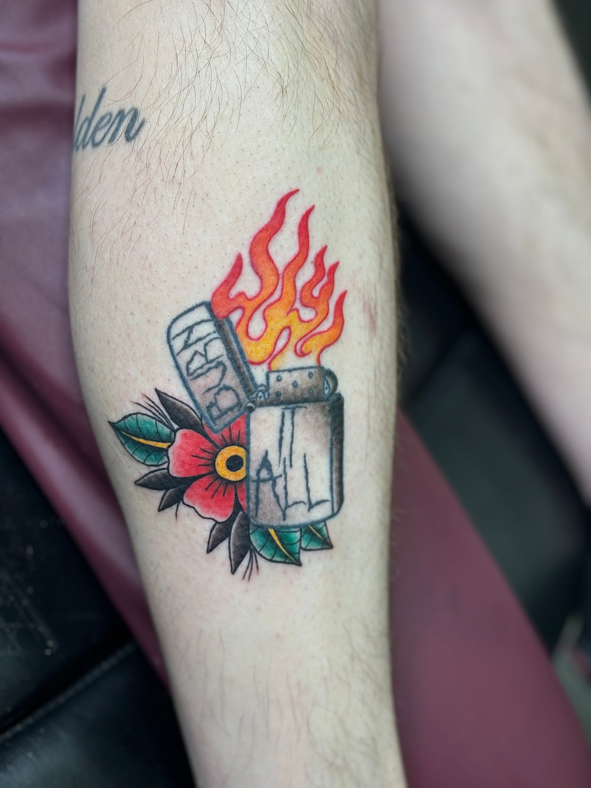 A tattoo of a lighter with flames and a flower on a person 's leg.