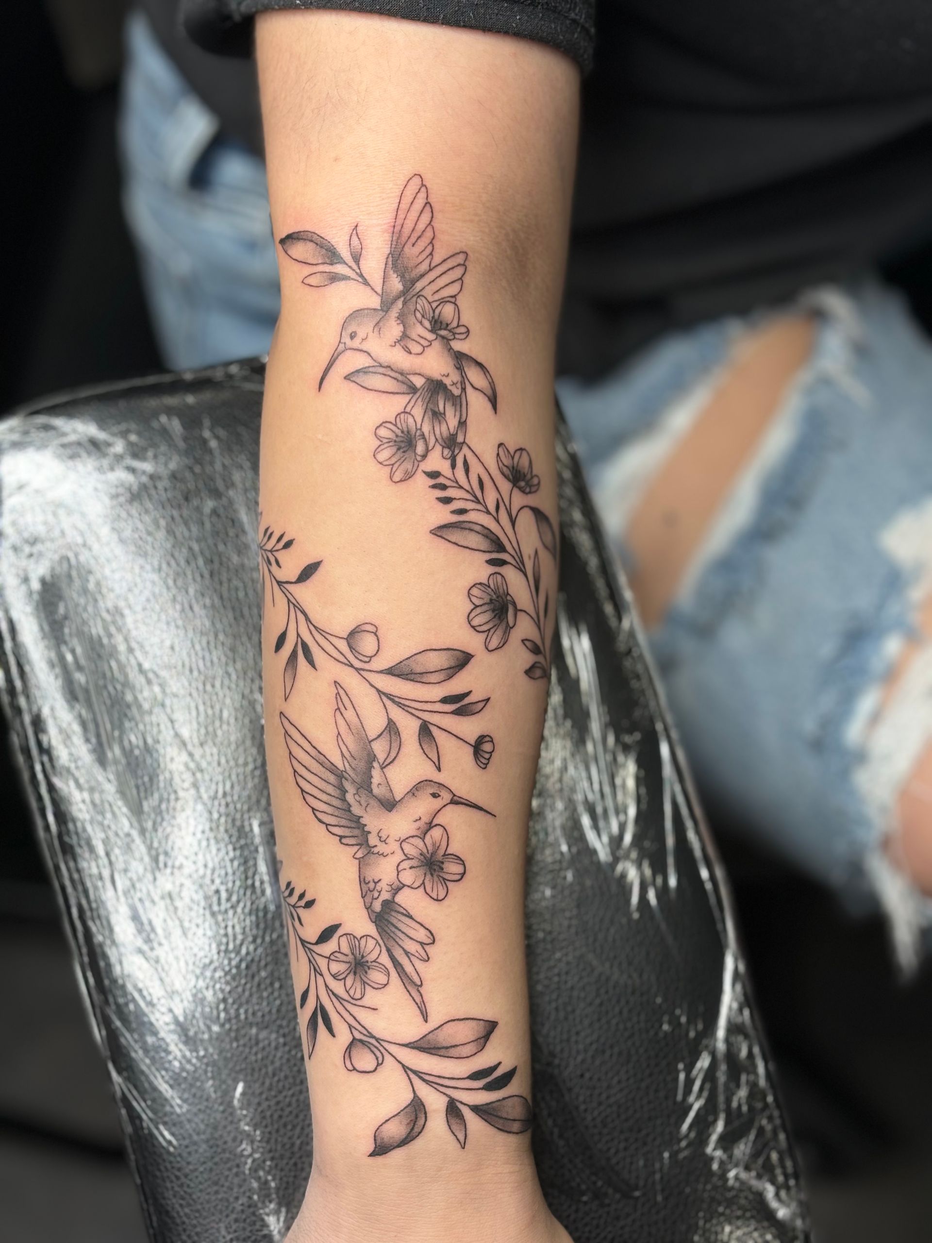 A woman has a tattoo of flowers and birds on her arm
