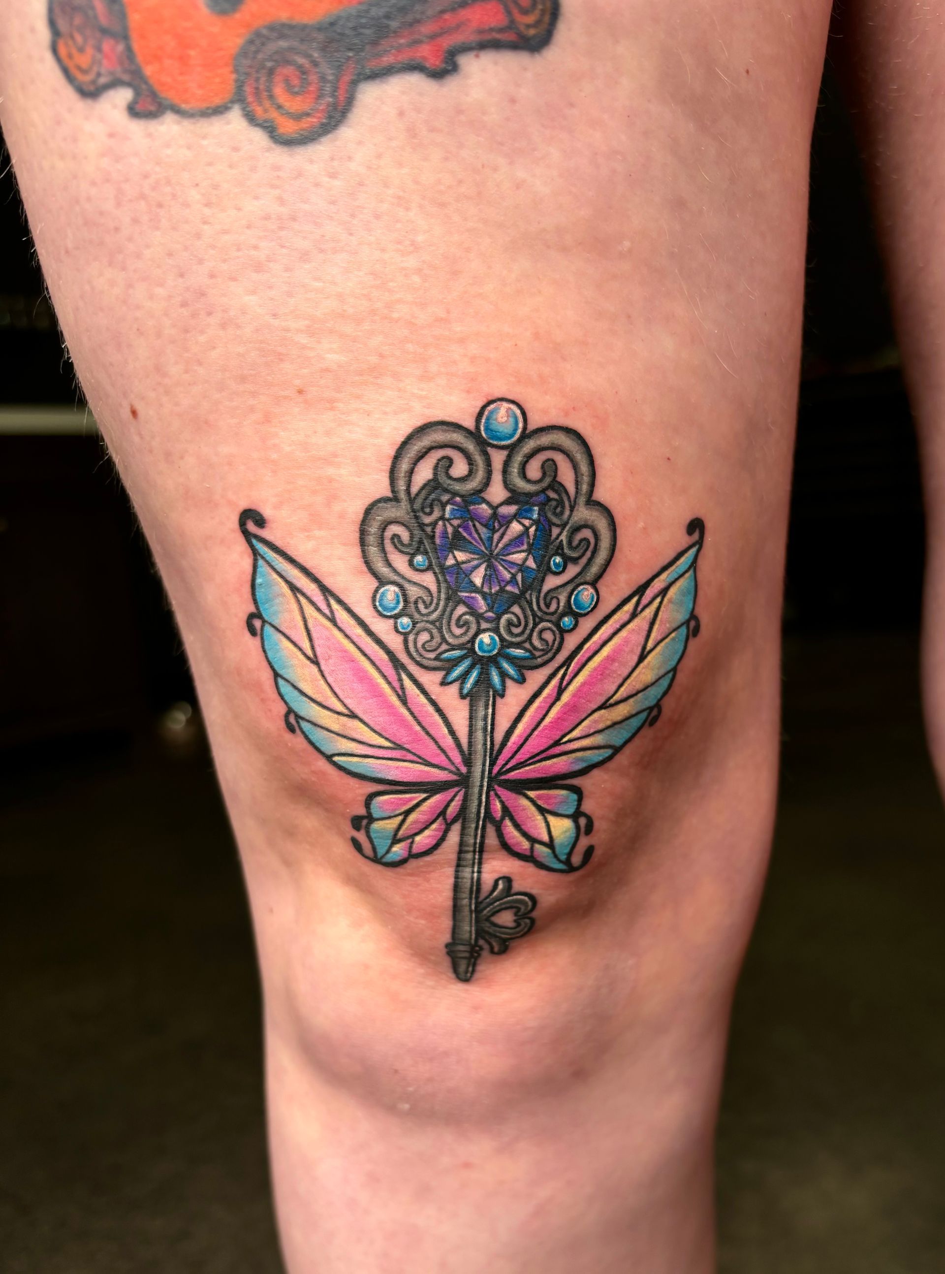 A woman has a tattoo of a key with wings on her knee