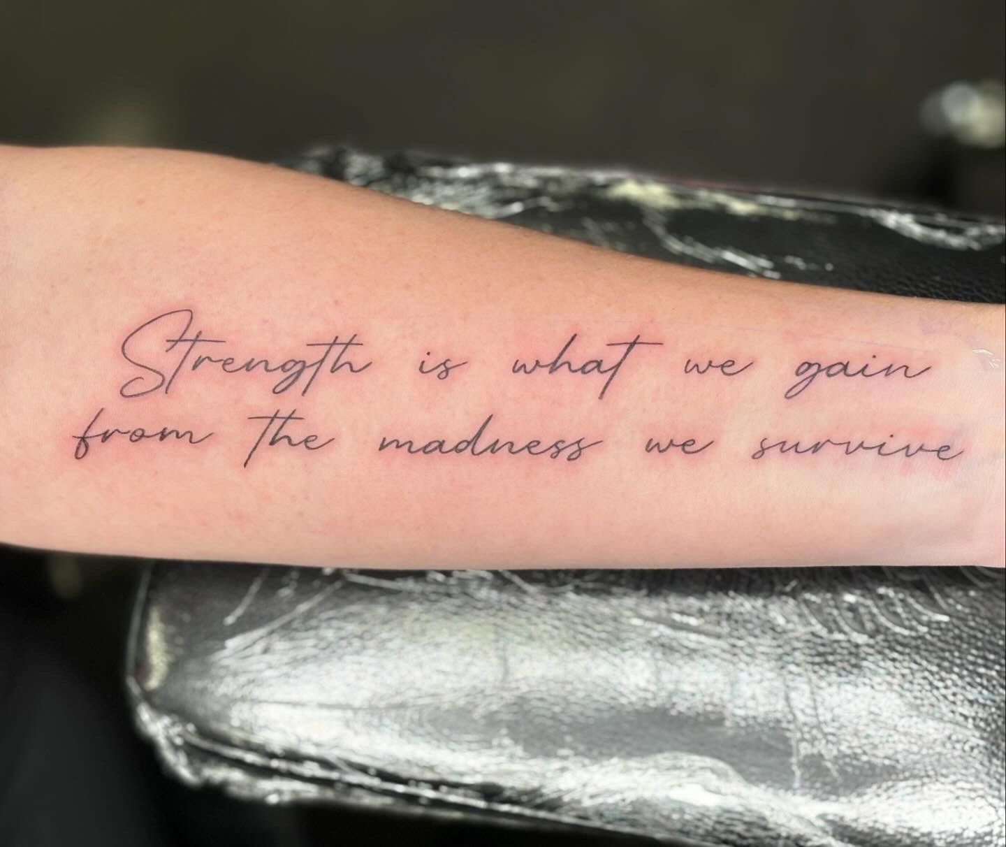 A tattoo on a person 's arm that says strength is what we gain from the madness we survive.