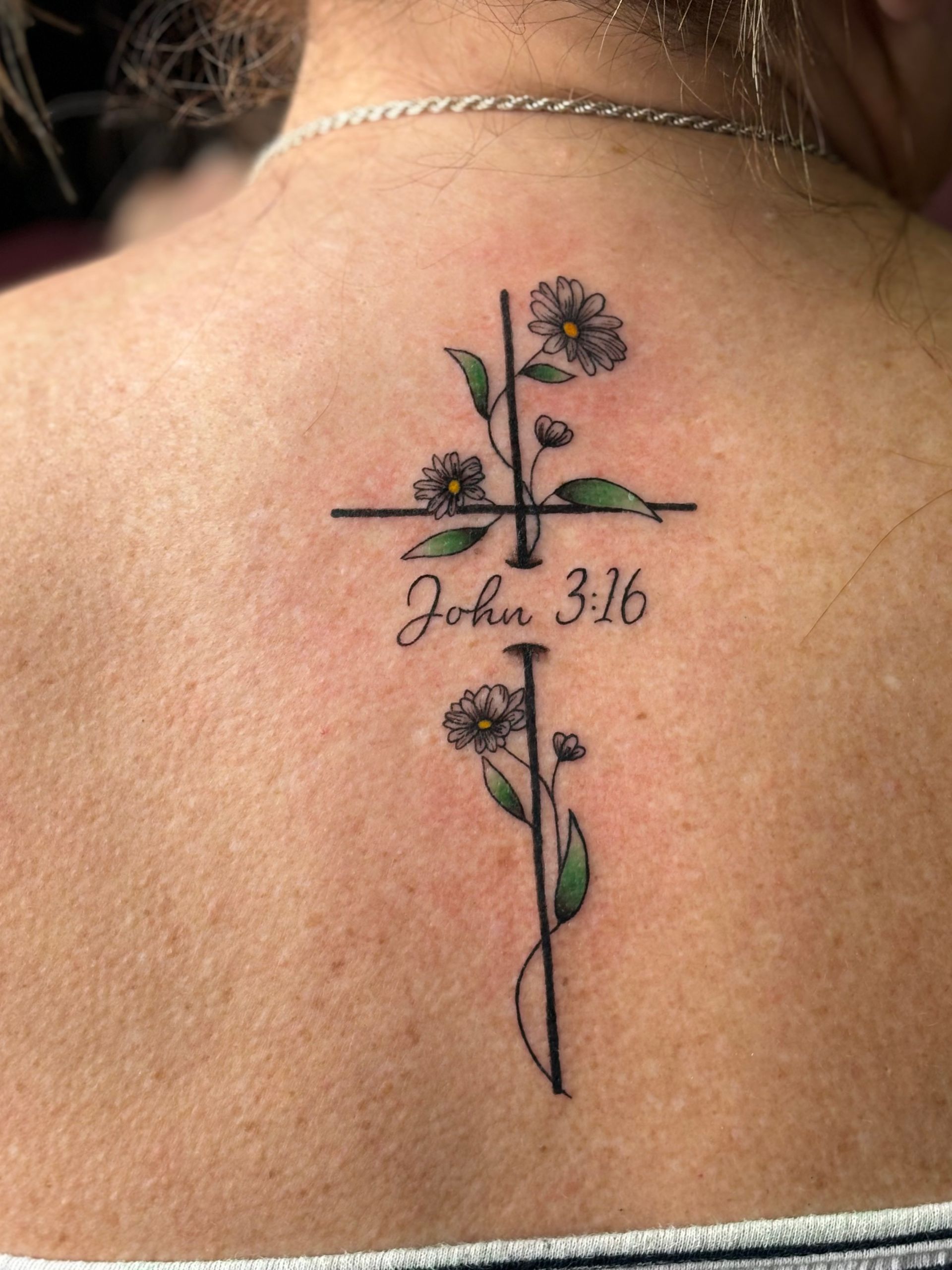 A woman has a tattoo of a cross and flowers on her back.