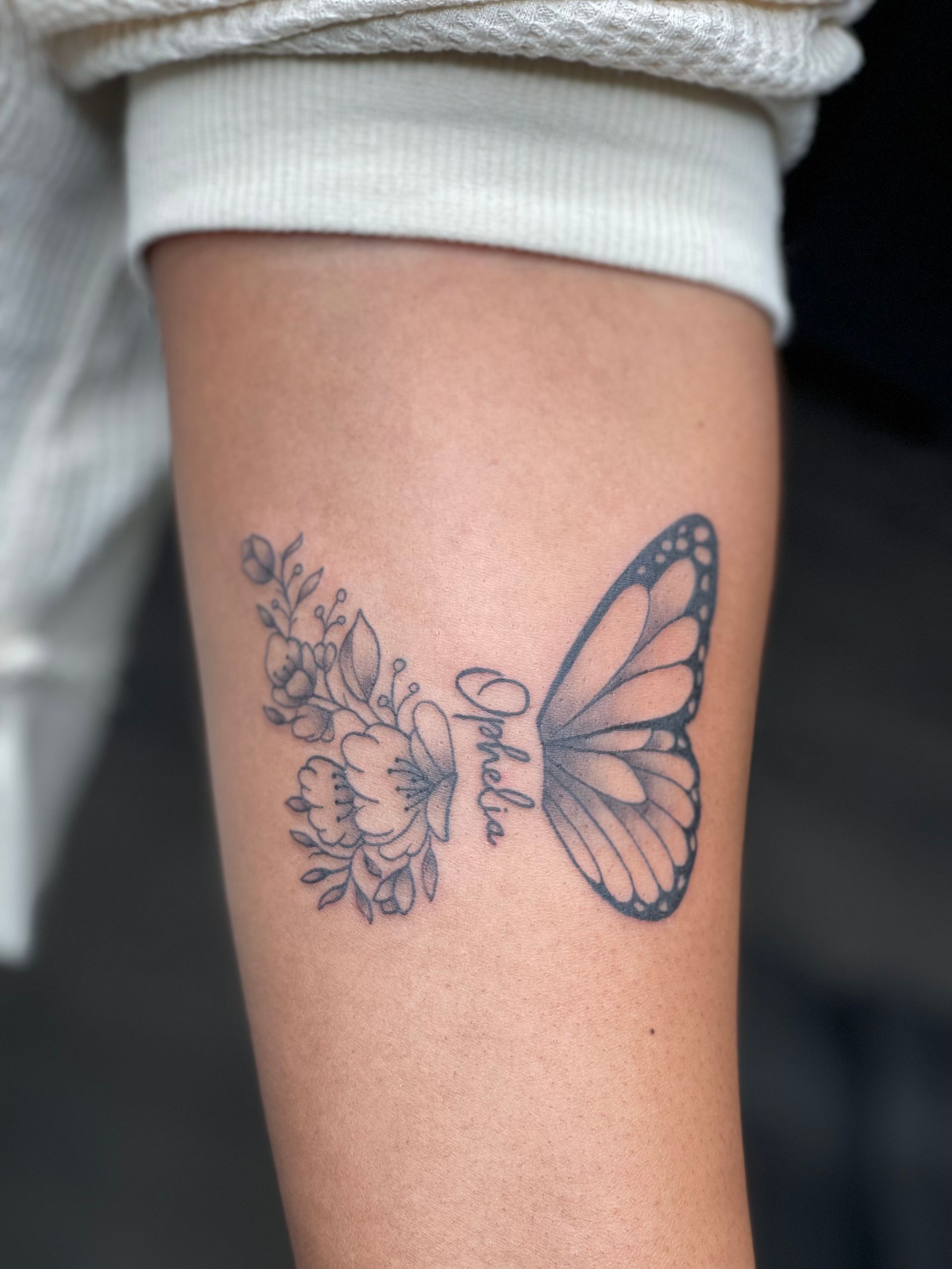 A woman has a tattoo of a butterfly and flowers on her arm