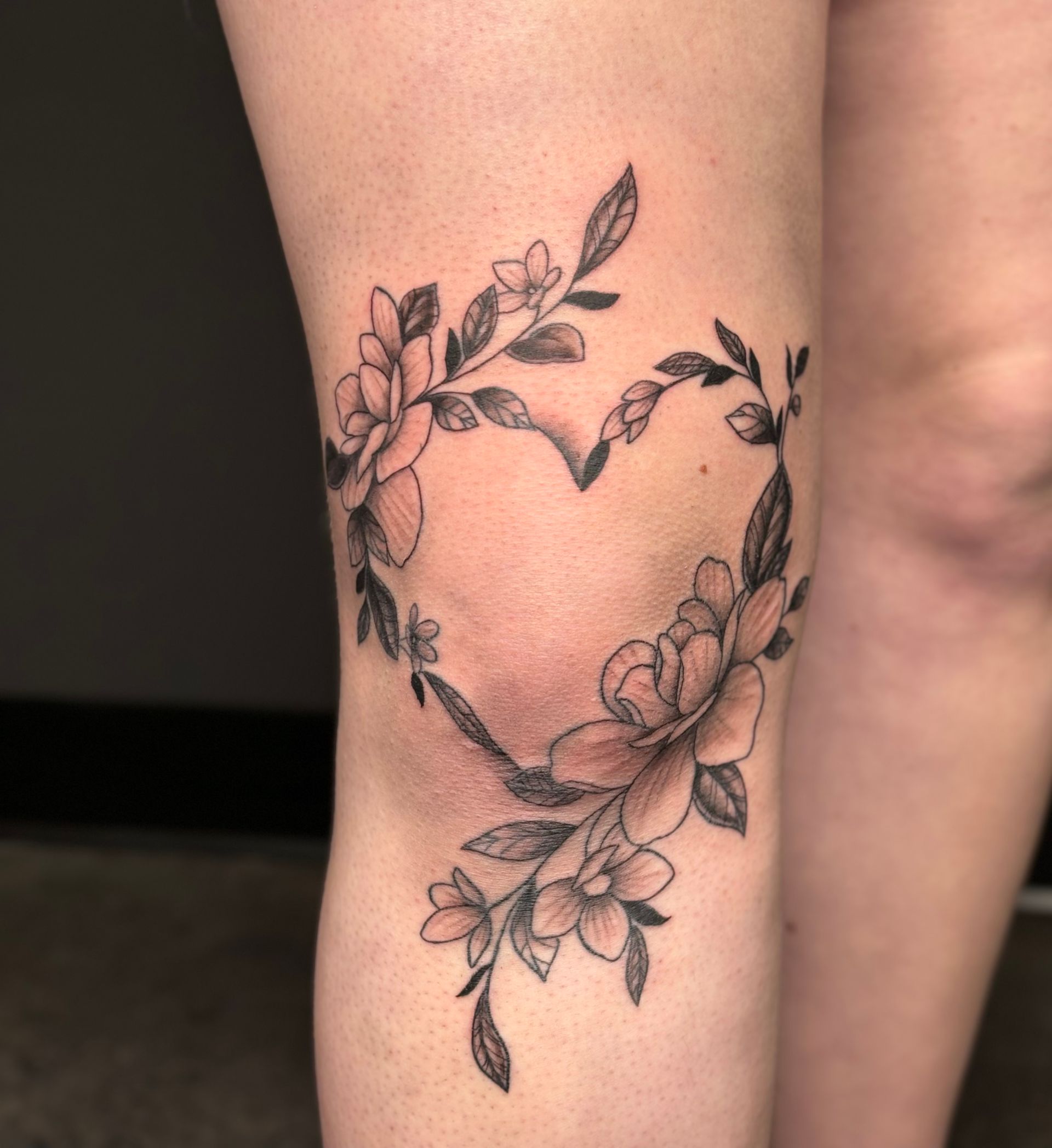 A woman has a heart shaped tattoo on her knee surrounded by flowers.