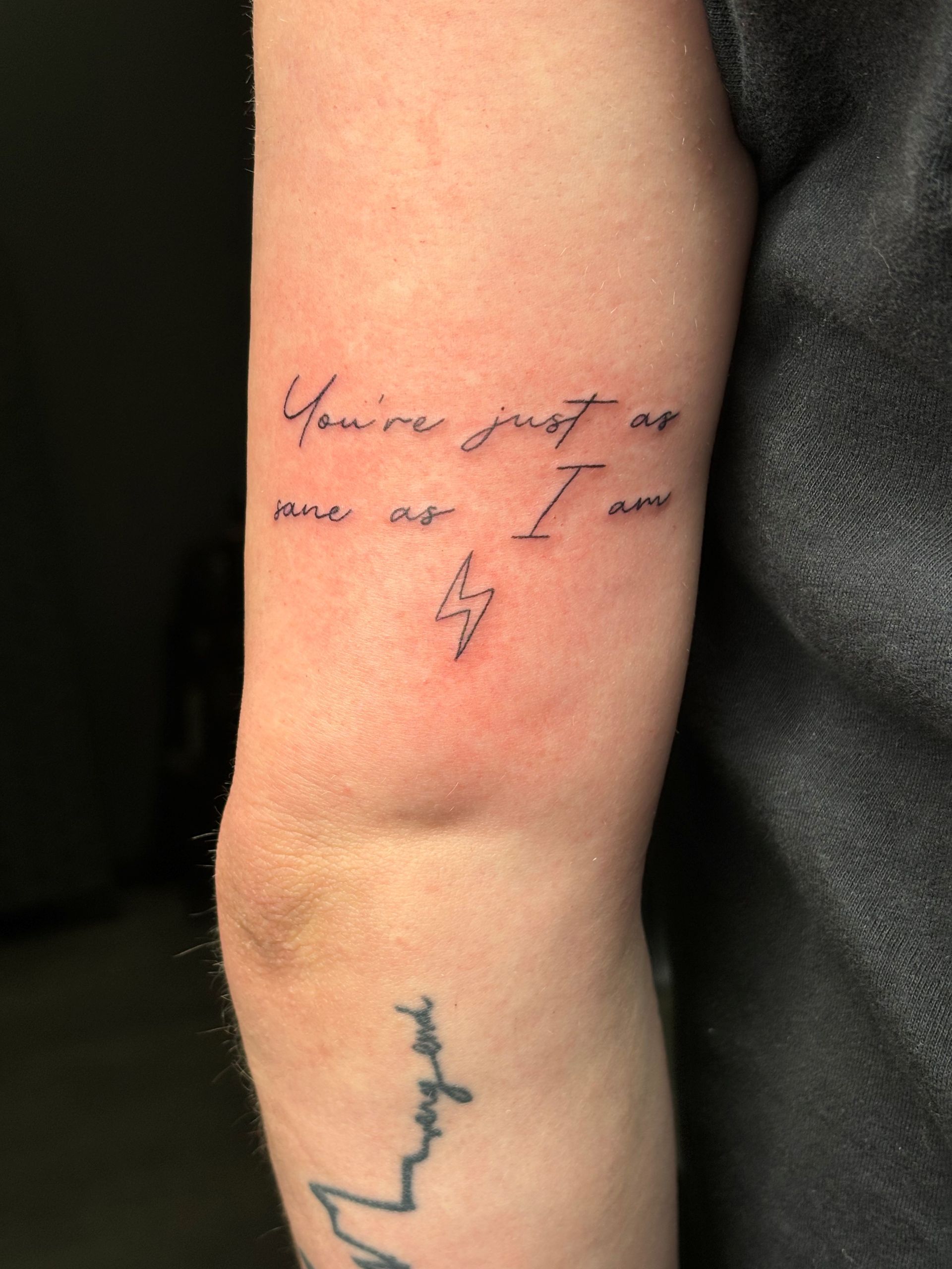 A person has a tattoo on their arm with text and a lightening bolt