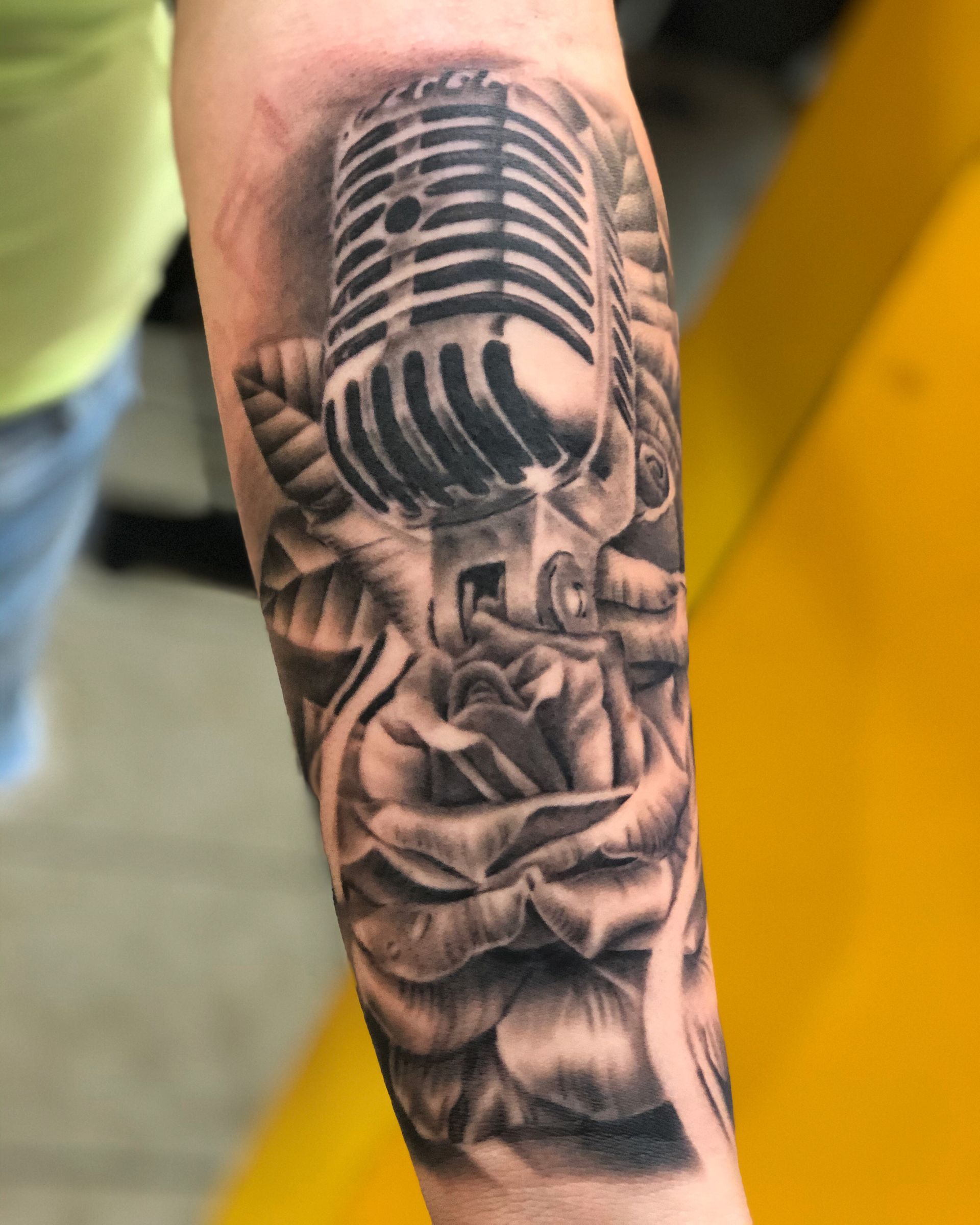 A person has a tattoo of a microphone and a rose on their forearm.