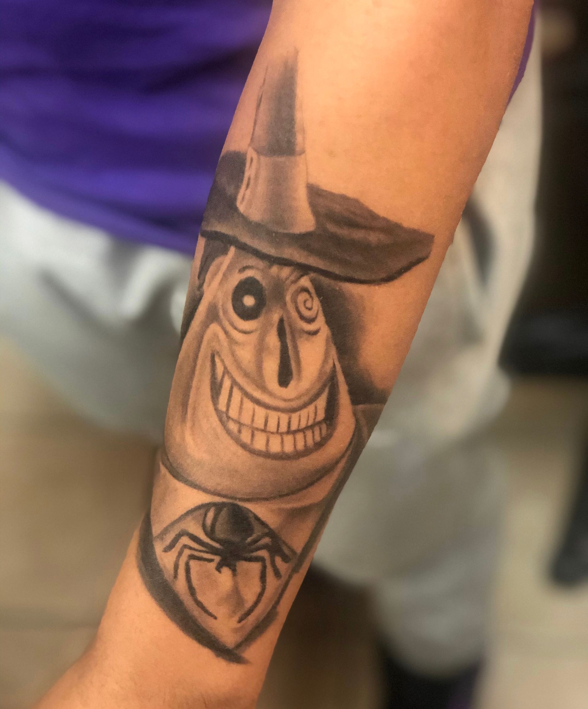 A person has a tattoo of a scarecrow and a spider on their forearm