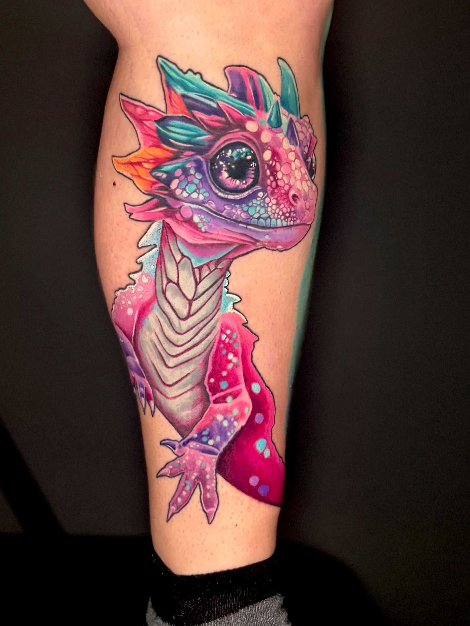 Colorful neon dragon tattoo on a calf, with pink, teal, and purple details