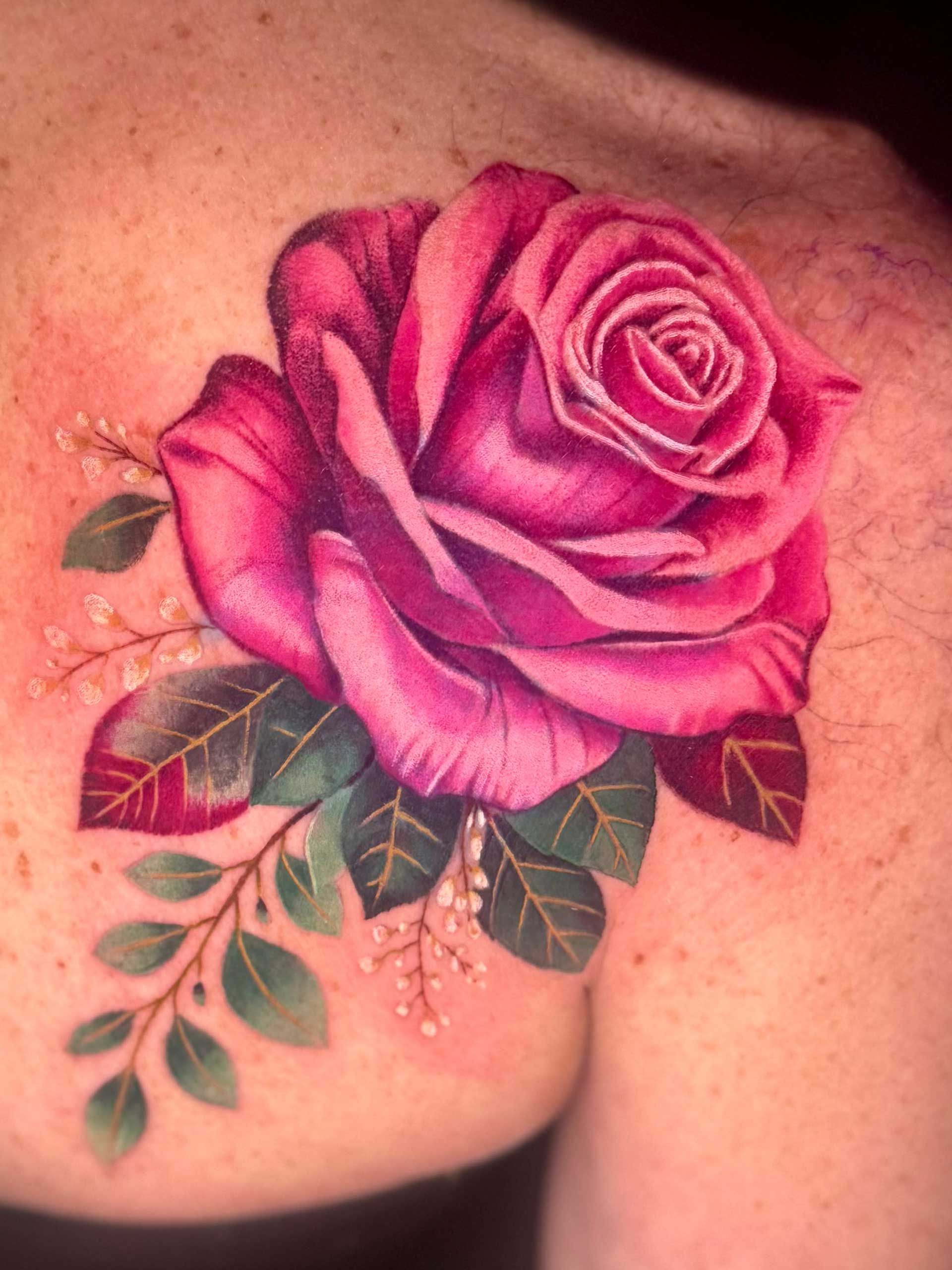 Pink rose tattoo on skin with green leaves and small floral accents
