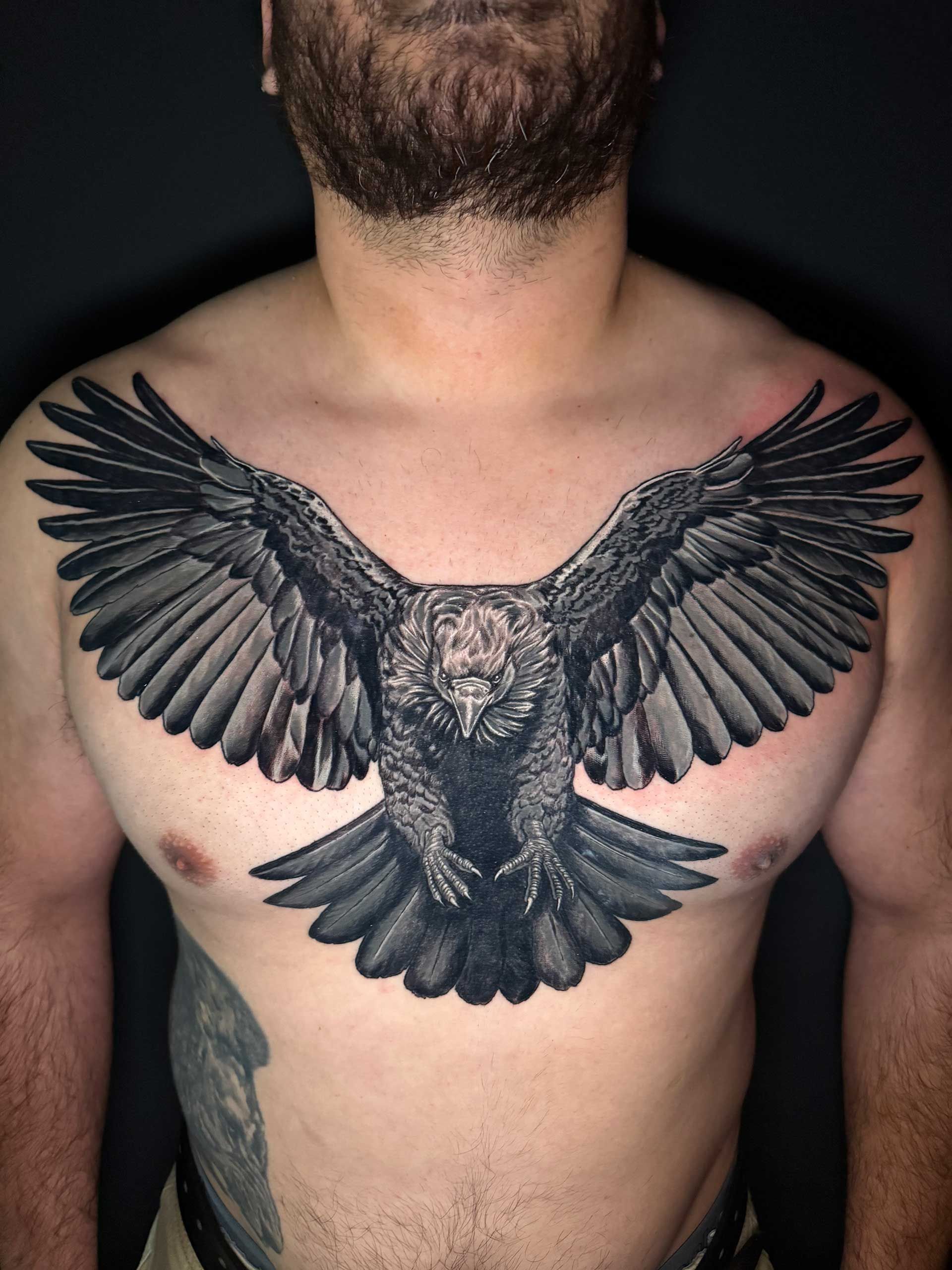 Black bird tattoo with outstretched wings across a shirtless chest