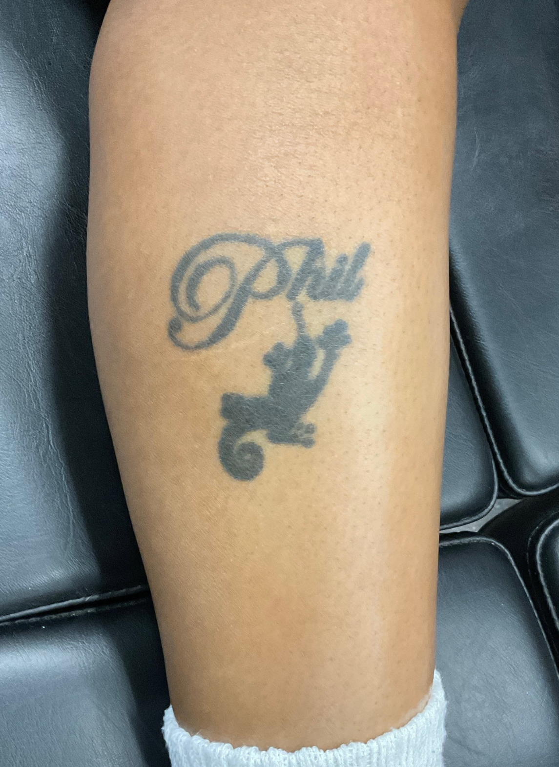 Tattoo on leg: Phil in cursive above a silhouette of a monkey, black ink.