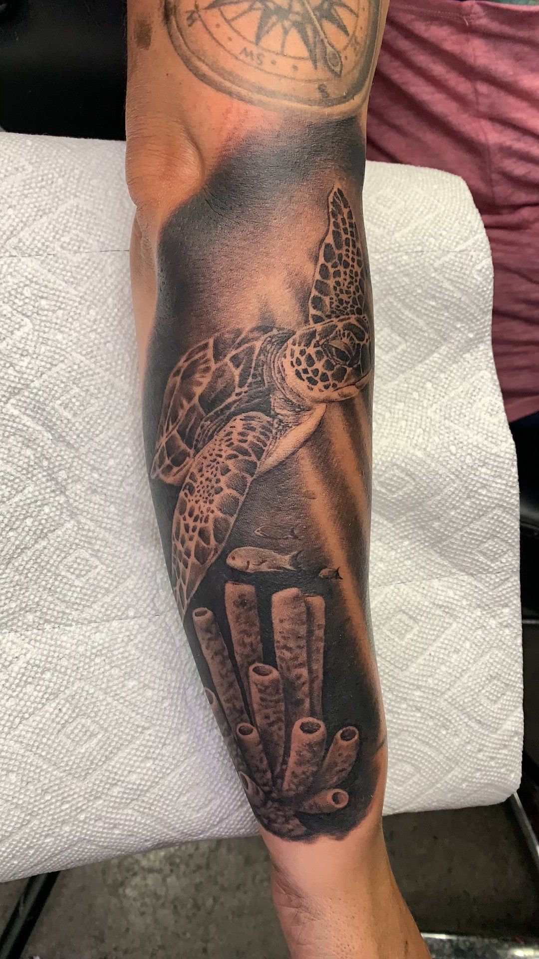 A black and white tattoo of a sea turtle on a person 's leg.