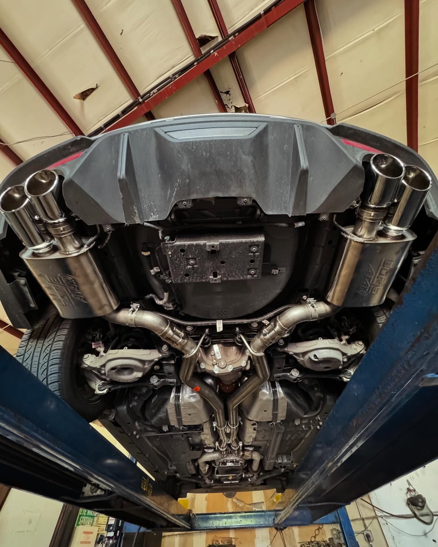 Underside of a car on a lift, showing a custom exhaust system. Stainless steel pipes and mufflers.