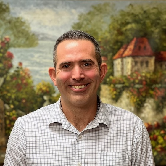 A man in a plaid shirt is smiling in front of a painting.