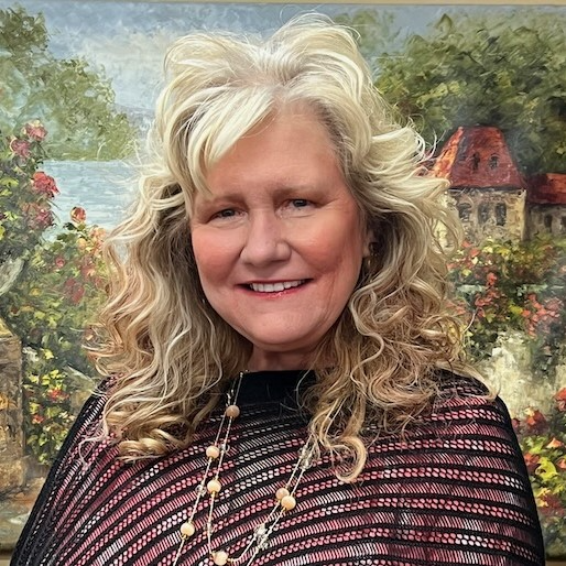 A woman with blonde hair is smiling in front of a painting.