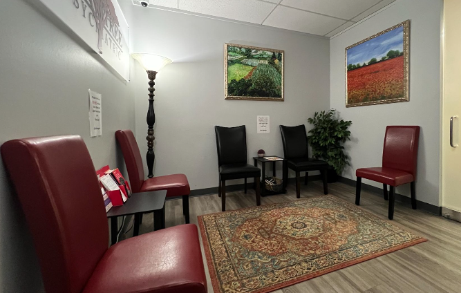 A waiting room with red chairs and a rug