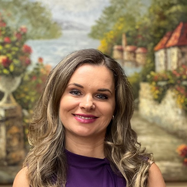 A woman in a purple shirt is smiling in front of a painting.