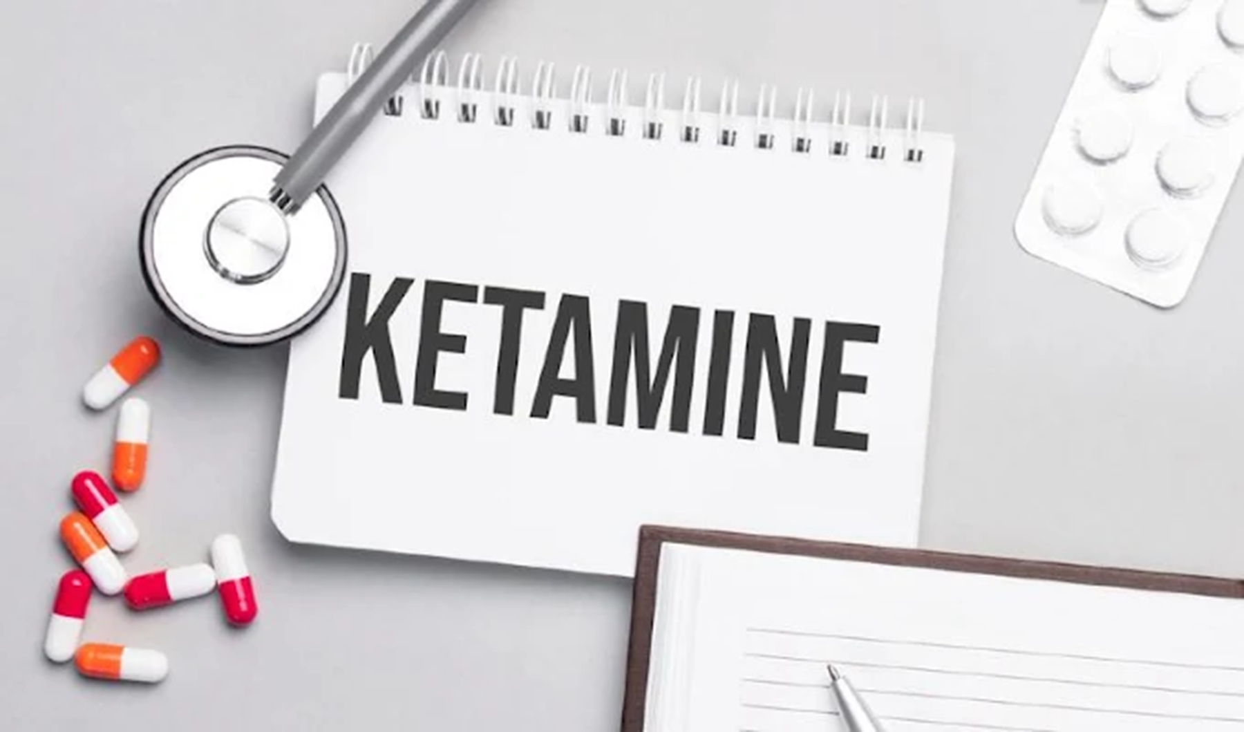a stethoscope over a notebook that says Ketamine. various types of pills displayed around the notebook.