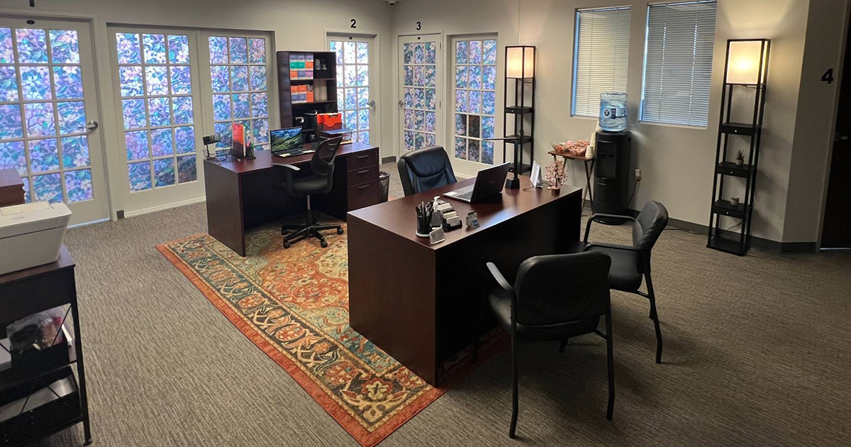 A room with a desk , chairs , and a rug.