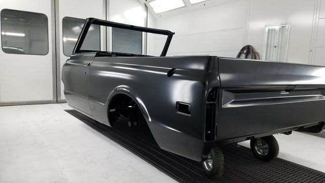 Black truck body in a paint booth, ready for assembly.