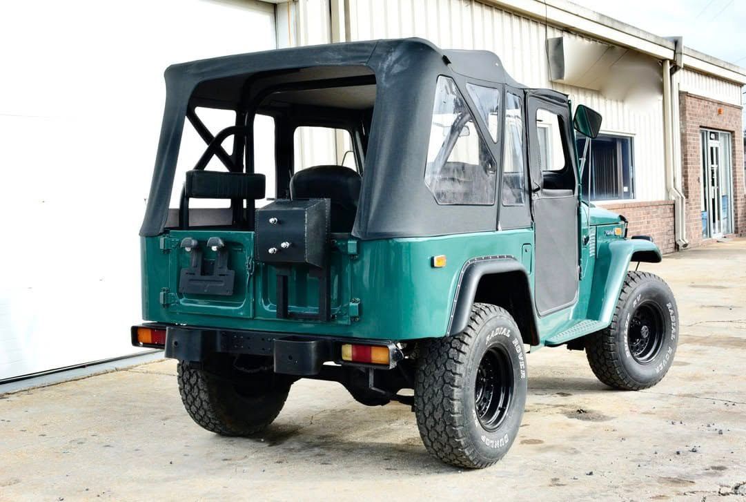 Green vintage Jeep with black soft top and tires, parked outside.