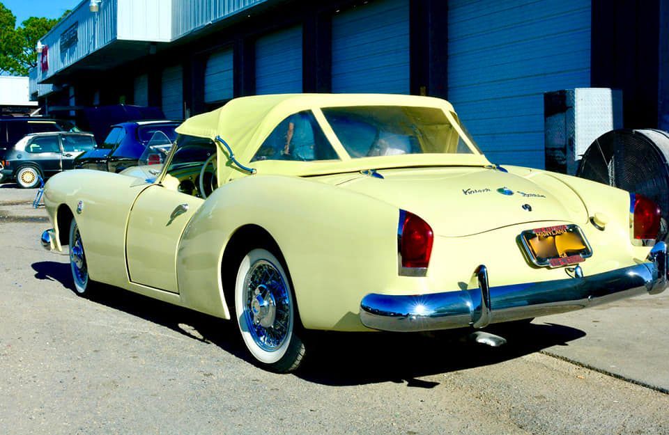 Pale yellow classic convertible with white-walled tires parked on pavement.
