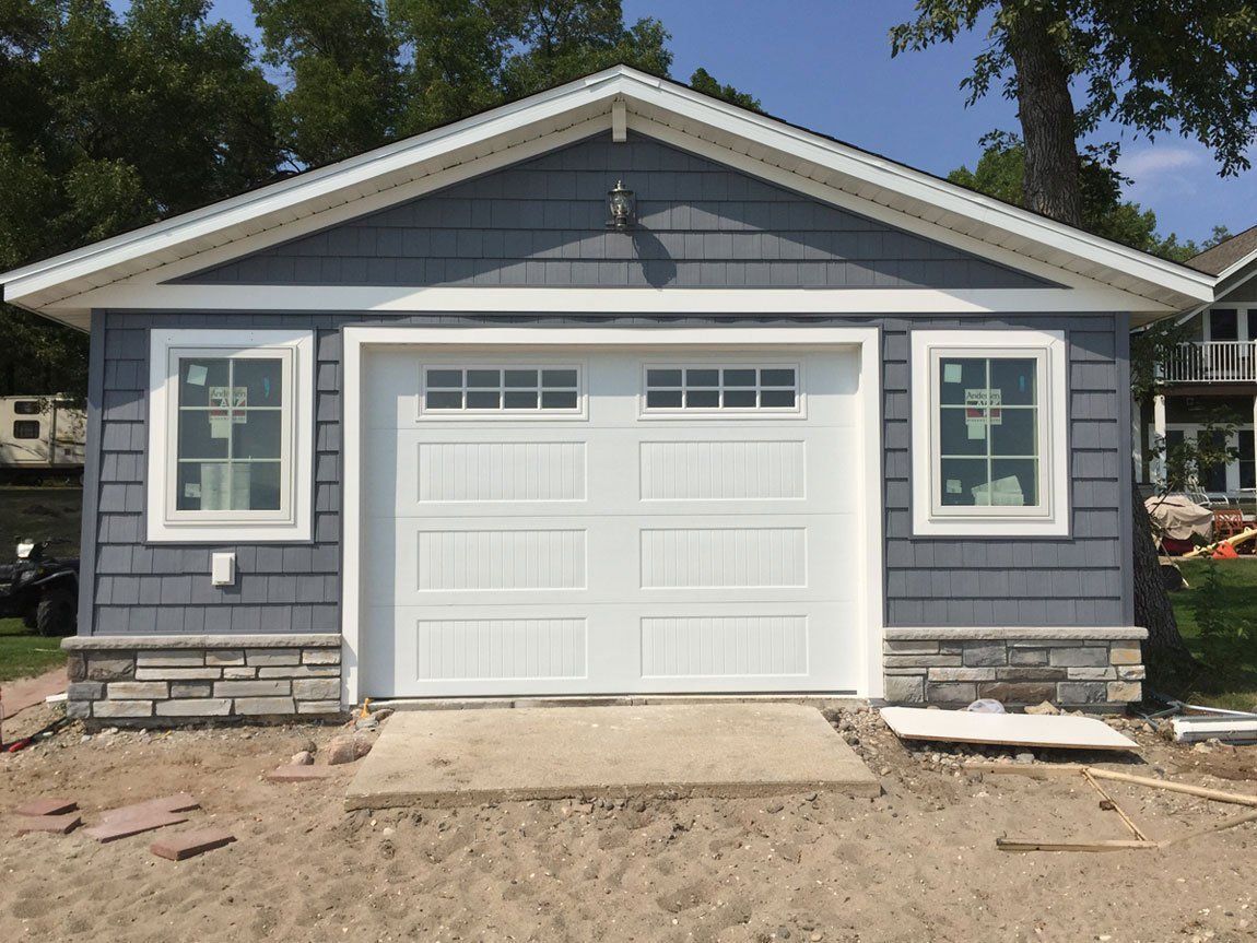 Gray house exterior with white garage door and front windows, under construction with unfinished dirt driveway