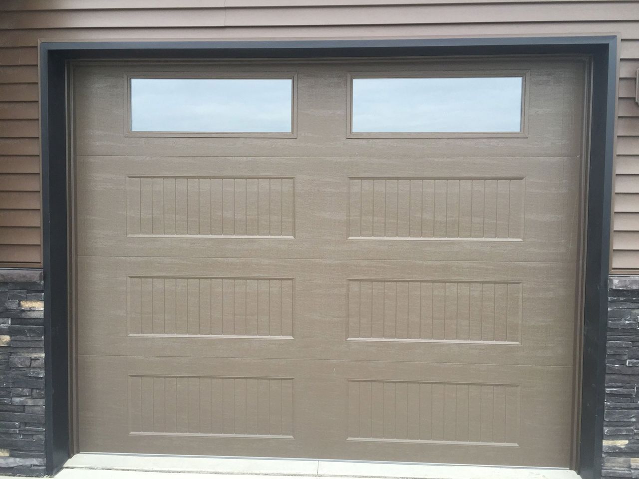 Tan garage door with two small windows and wood siding on either side
