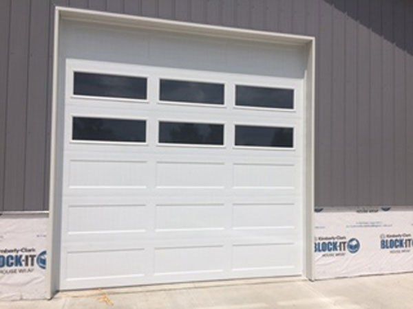 White garage door with three rows of windows on a gray building exterior