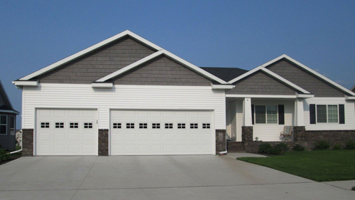 White three-car garage door with small windows on a brick house exterior