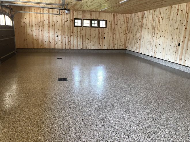 Empty wood-paneled basement with speckled floor and small windows along the back wall