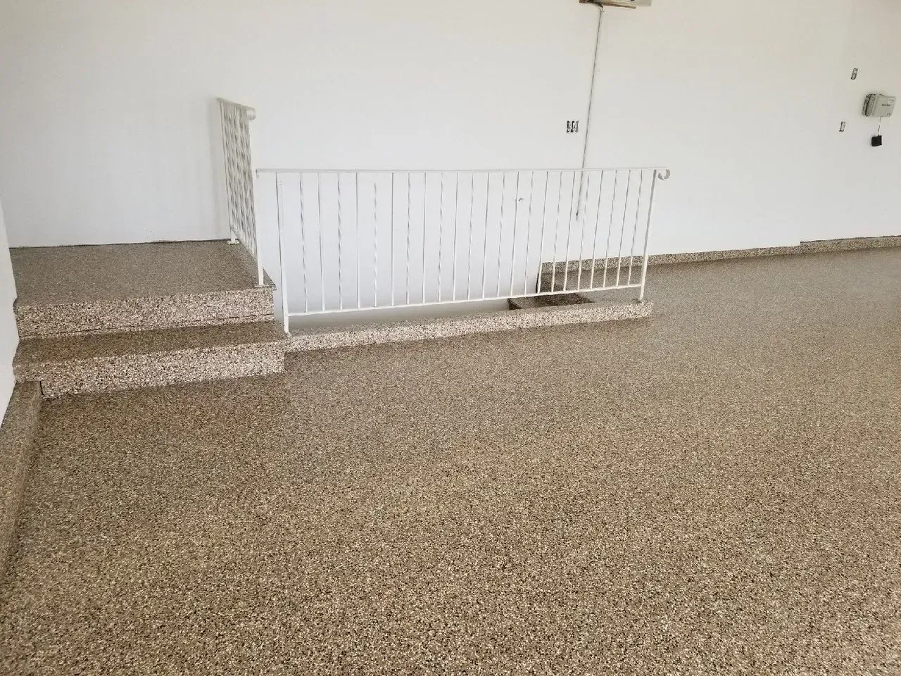 Empty room with speckled flooring, white walls, and a small stairway beside a railing.