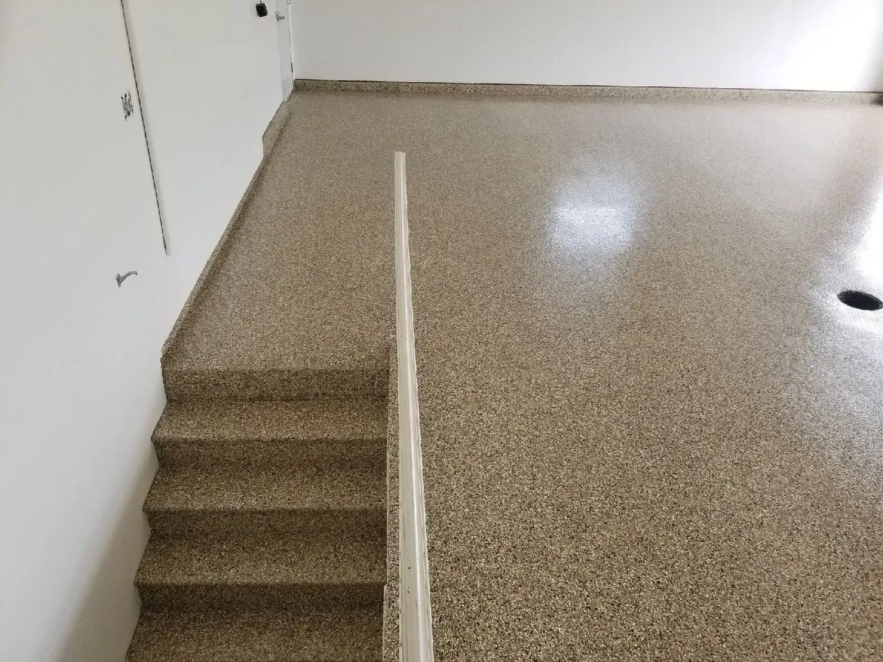 Indoor stairwell with a small step down and speckled terrazzo floor at the landing