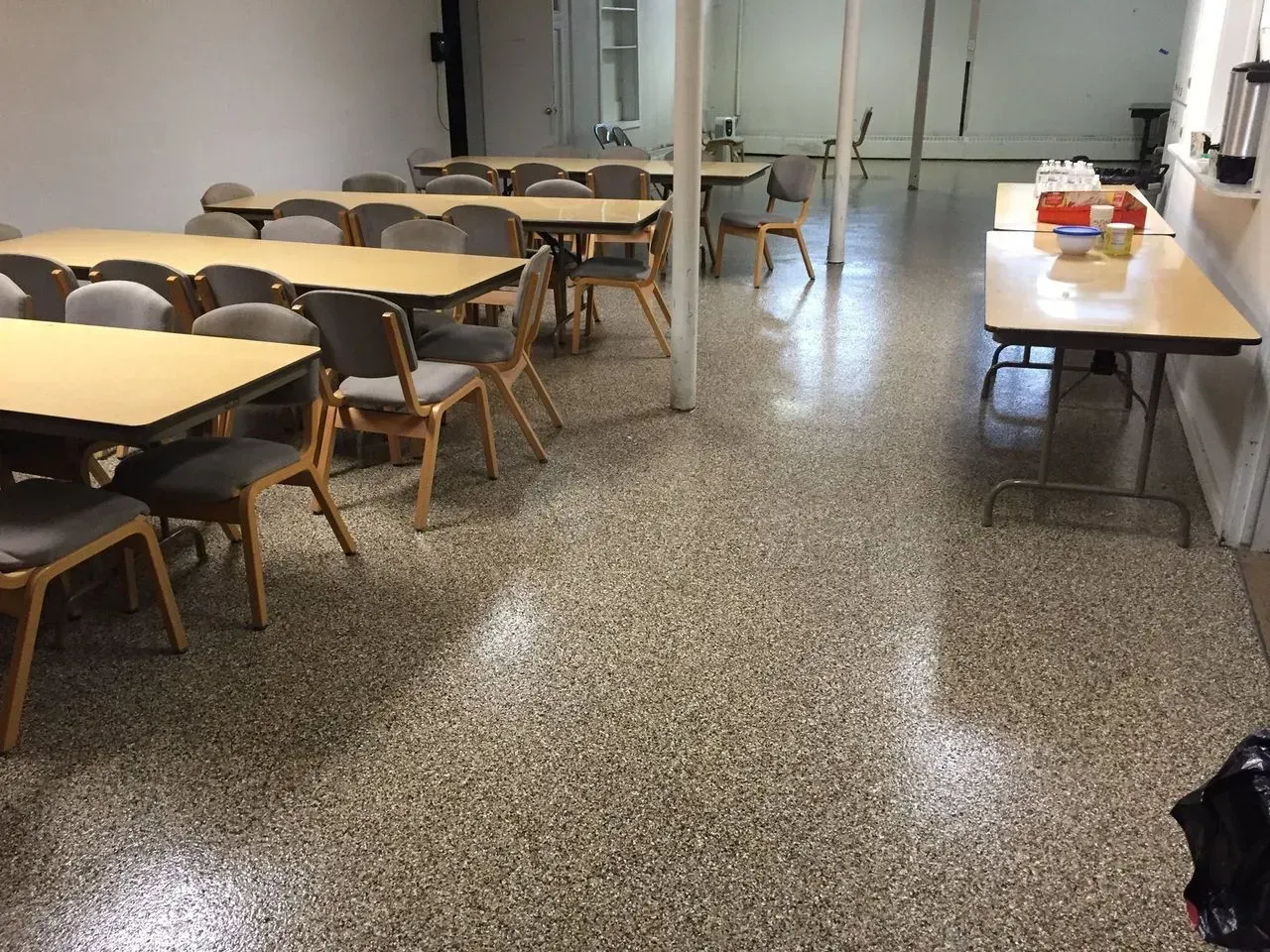 Empty classroom with tables, chairs, and a speckled tile floor under bright lights