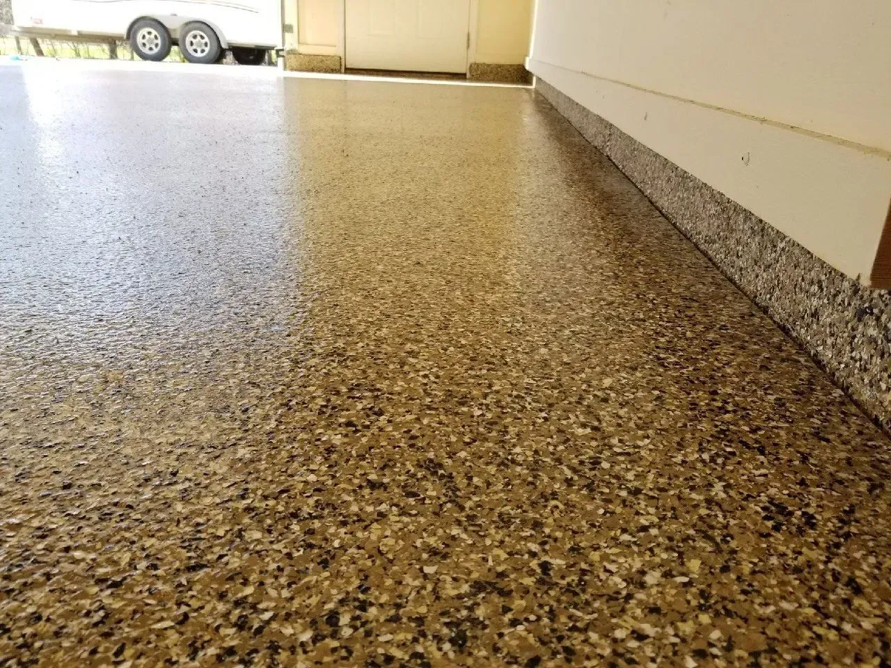 Speckled terrazzo floor beside a wall, with a doorway and parked trailer in the background.