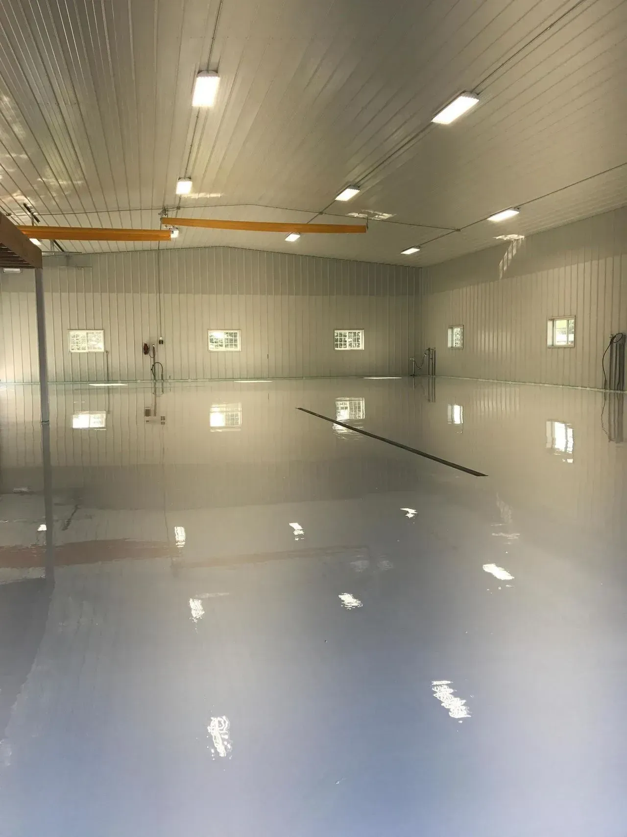 Empty white warehouse with a glossy floor and overhead lights reflected on the surface
