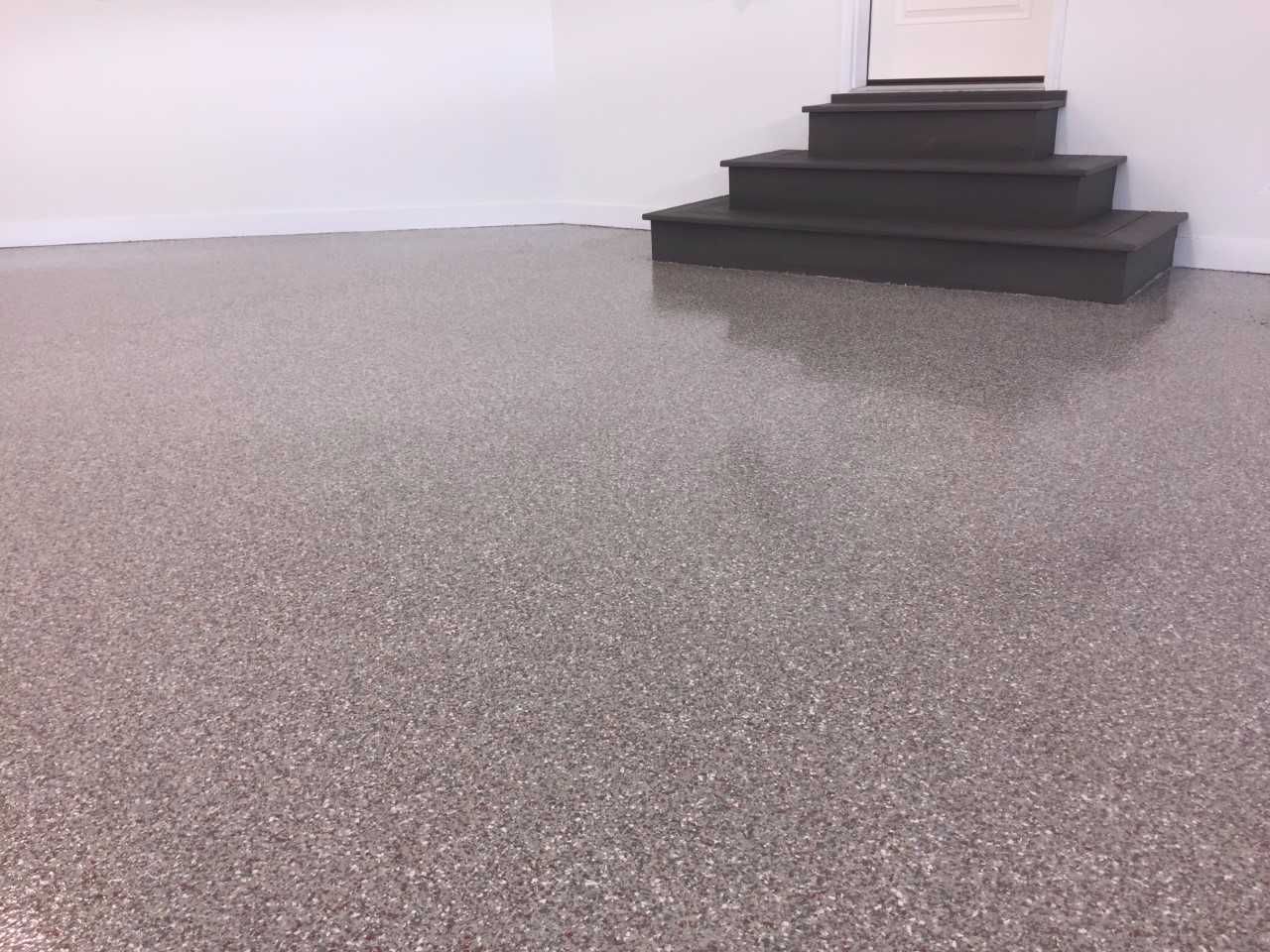 Empty gray speckled floor with a small black staircase against a white wall