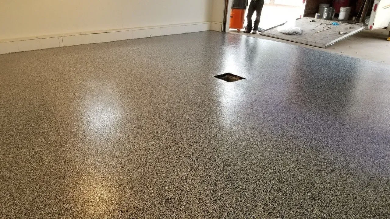 Speckled gray epoxy floor in a garage with a small drain near the center.