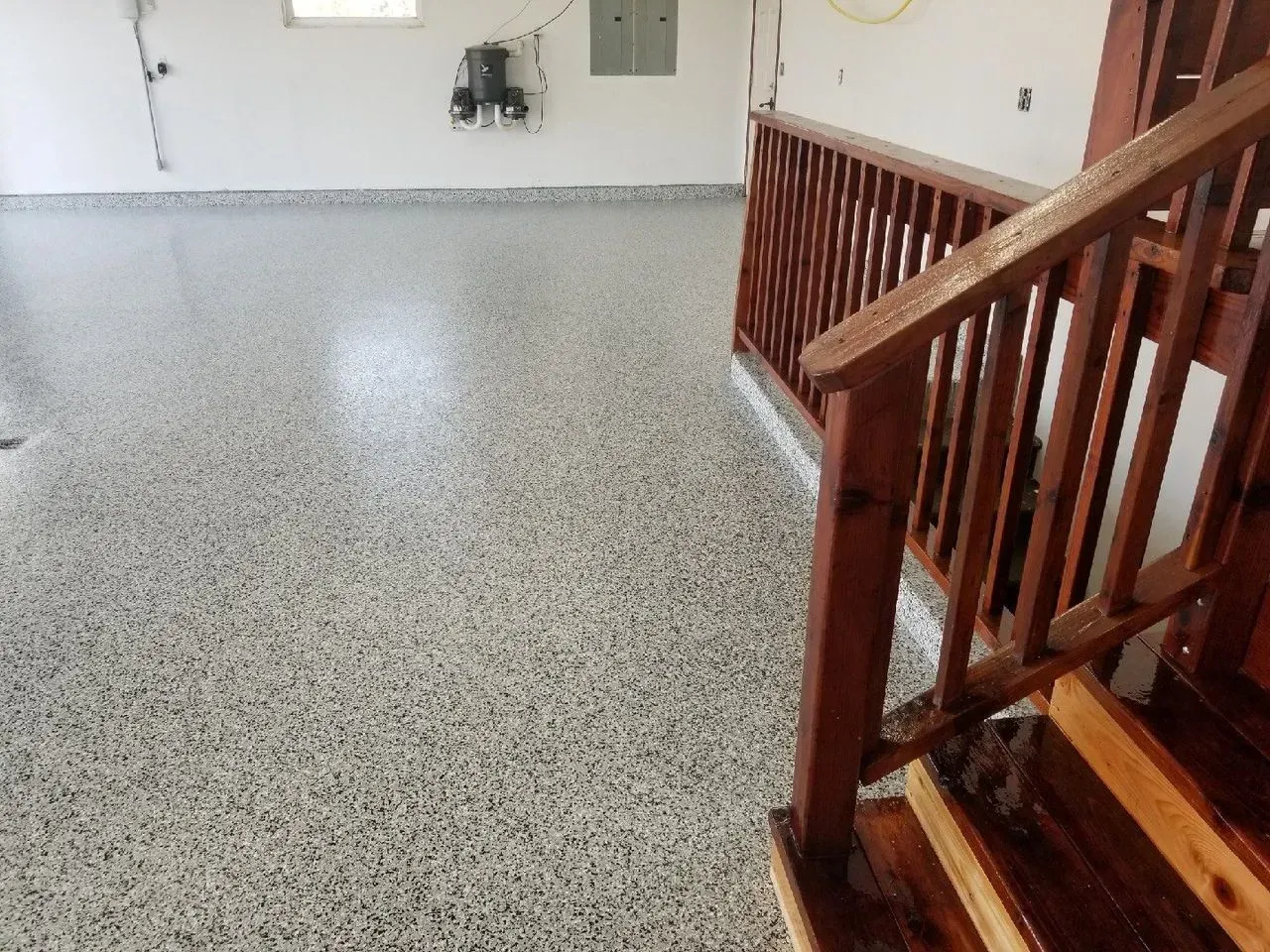 Empty room with speckled floor, white walls, and wooden staircase railing on the right