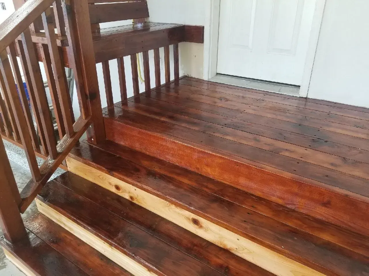 Wooden porch deck with steps, railing, and a white door in the background